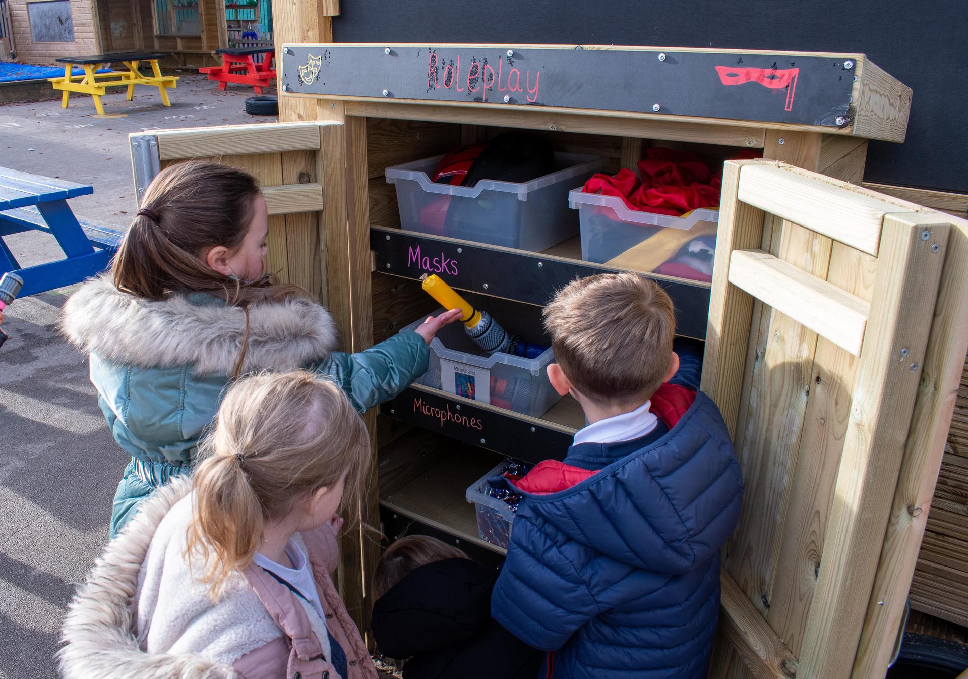 Three school children taking provisions out of a wooden Acorn Self Select Storage Unit