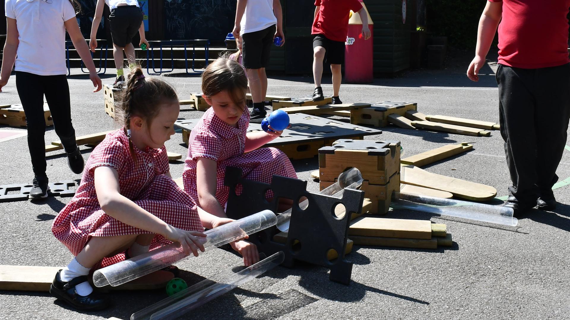 Two little girls are connecting the plastic pipes together to create a complete water play circuit.