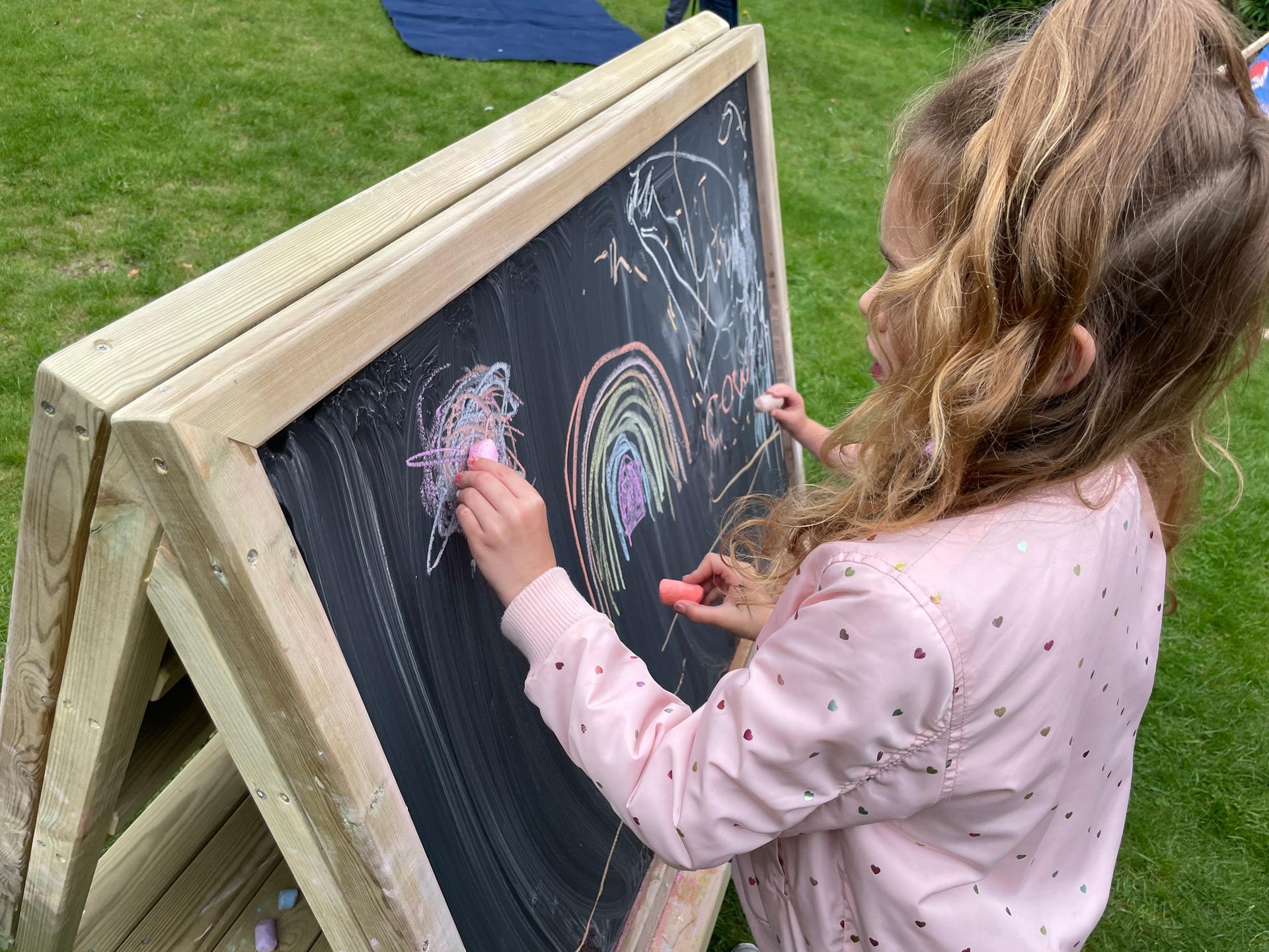 Children drawing on a wooden, chalkboard easel on wheels.
