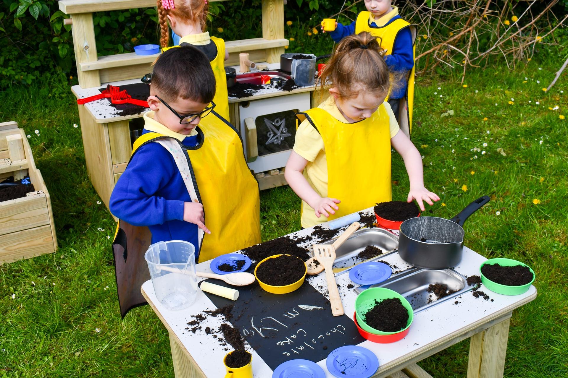 An EYFS boy and girl are using messy play resources on the Mud Kitchen Island.