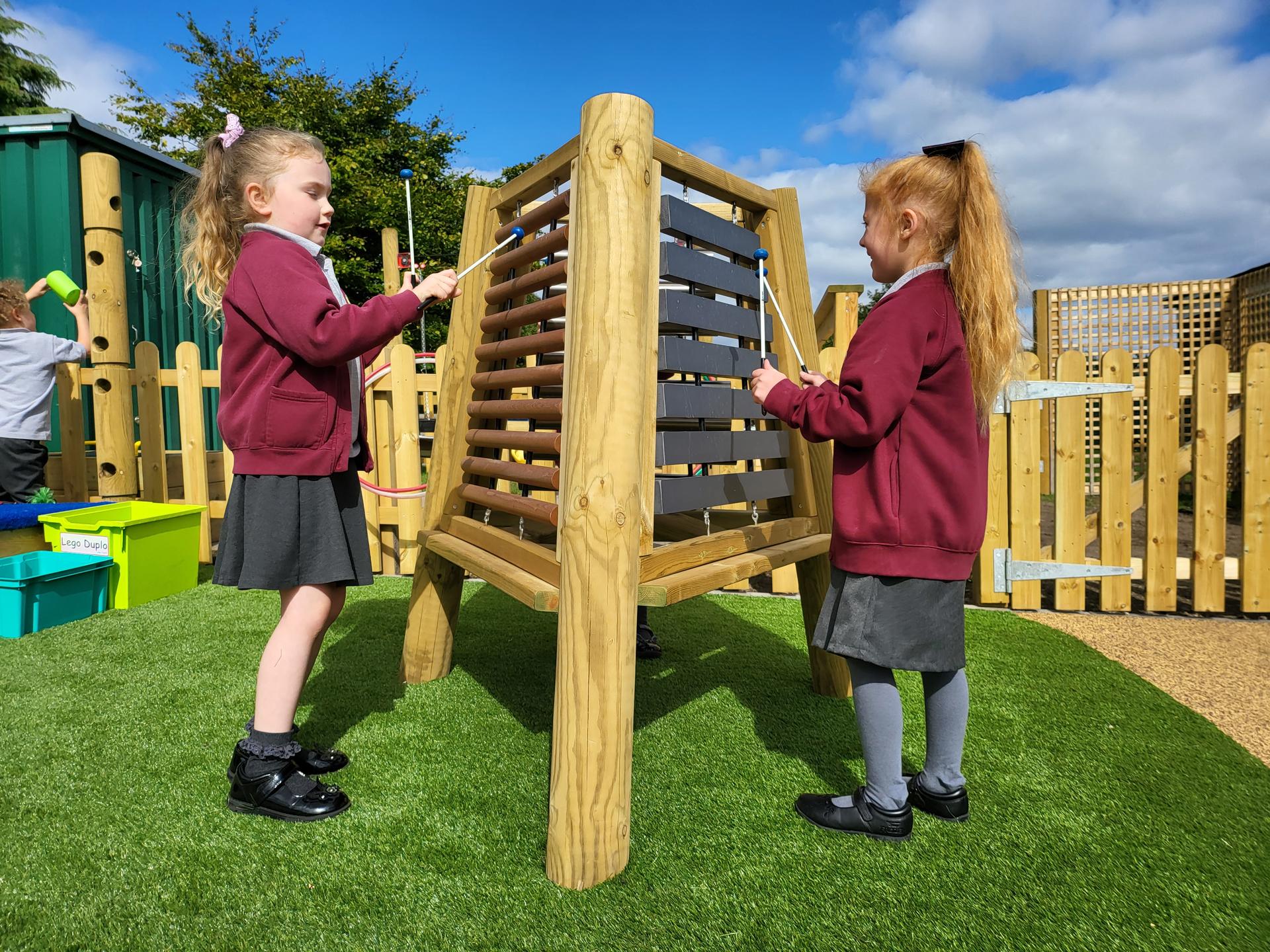 A musical triad being played by two girls on artificial grass.