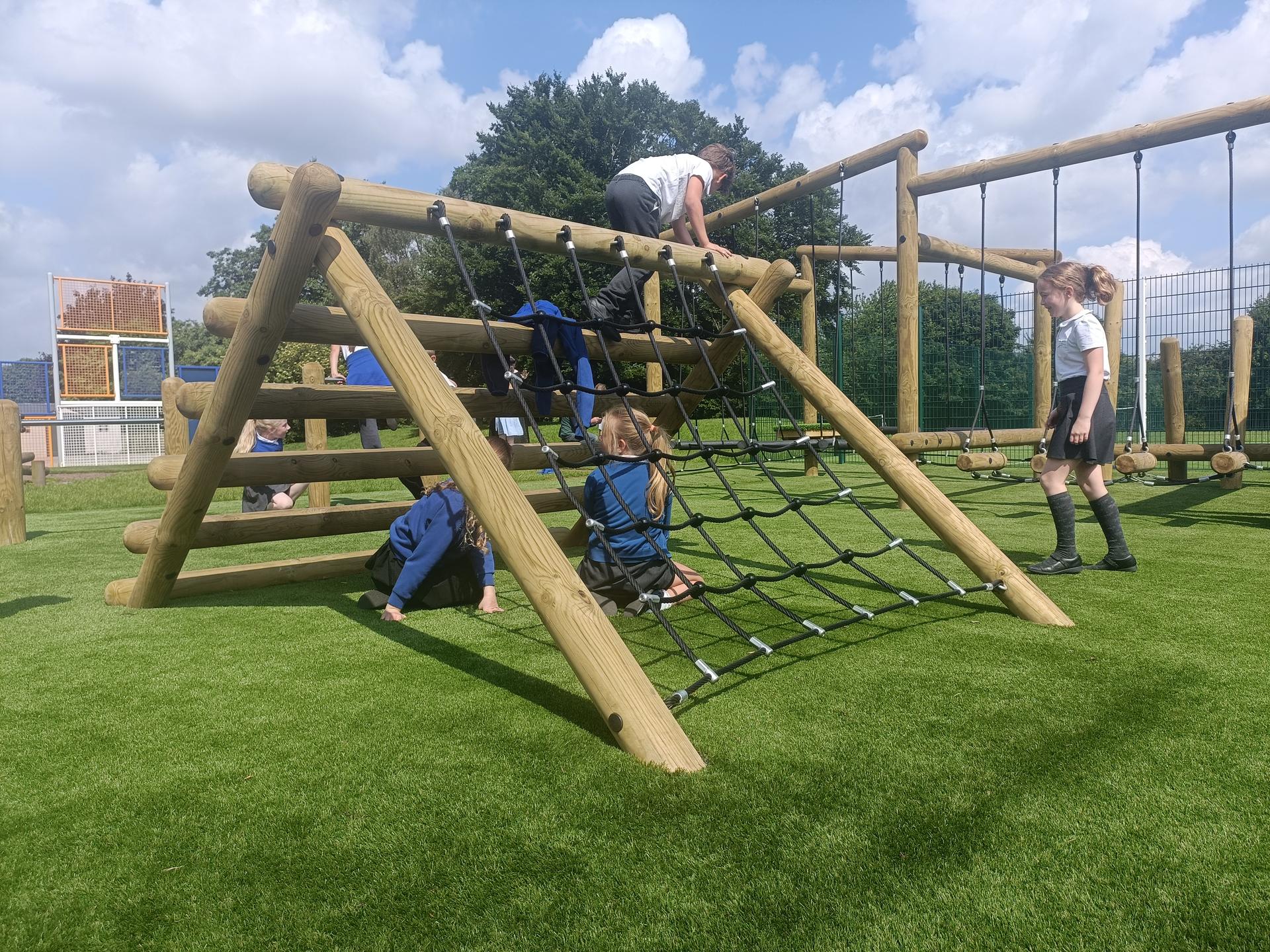 A group of children are sat underneath the Forest Log Climber with a net, as a child climbs over it.