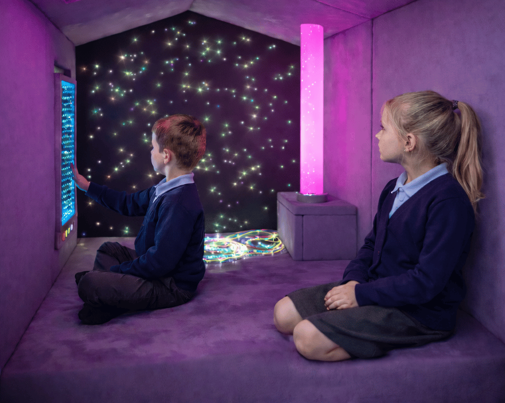 A girl and a boy are sat within the sensory nook, looking around at all of the interactive features.