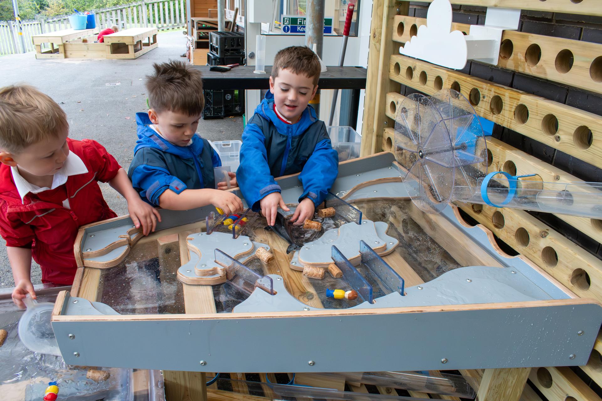 A full view of the damming station next to the moveable water wall. Three children placing toys in the damming station.