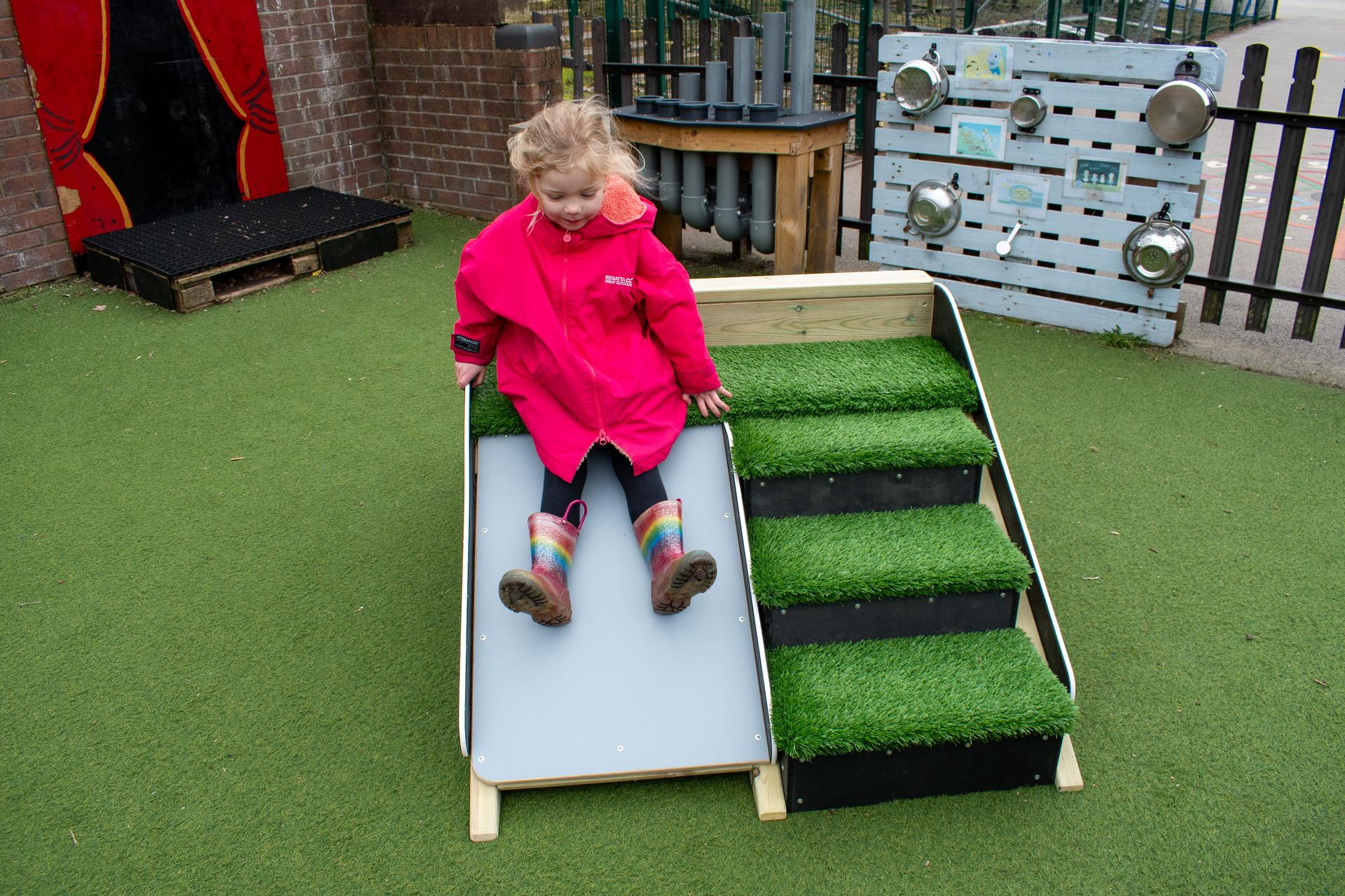 A child sliding down the a-frame, placed on a nursery playground.