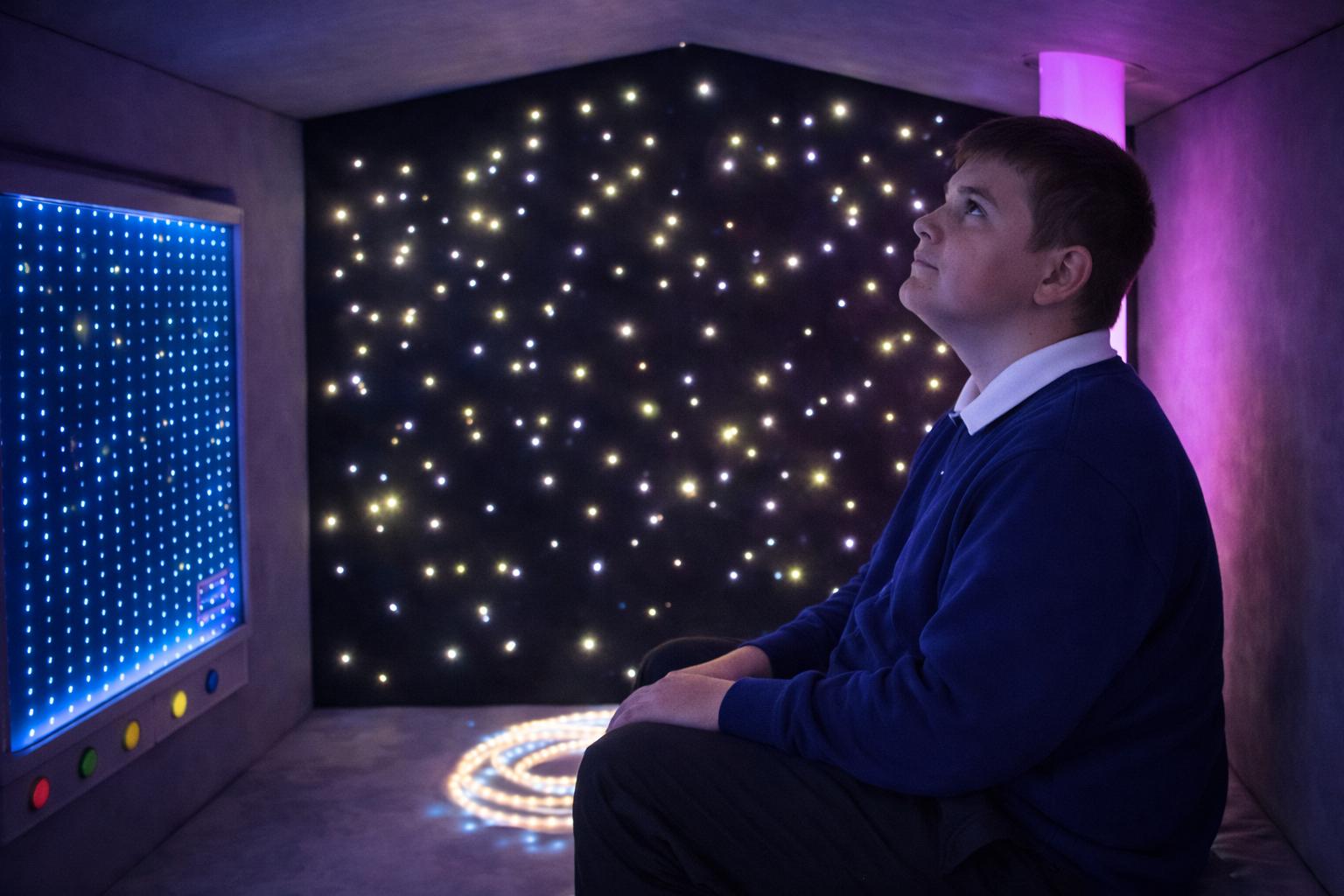 A boy is looking up at the ceiling, admiring the sensory lights that are beaming down on him.