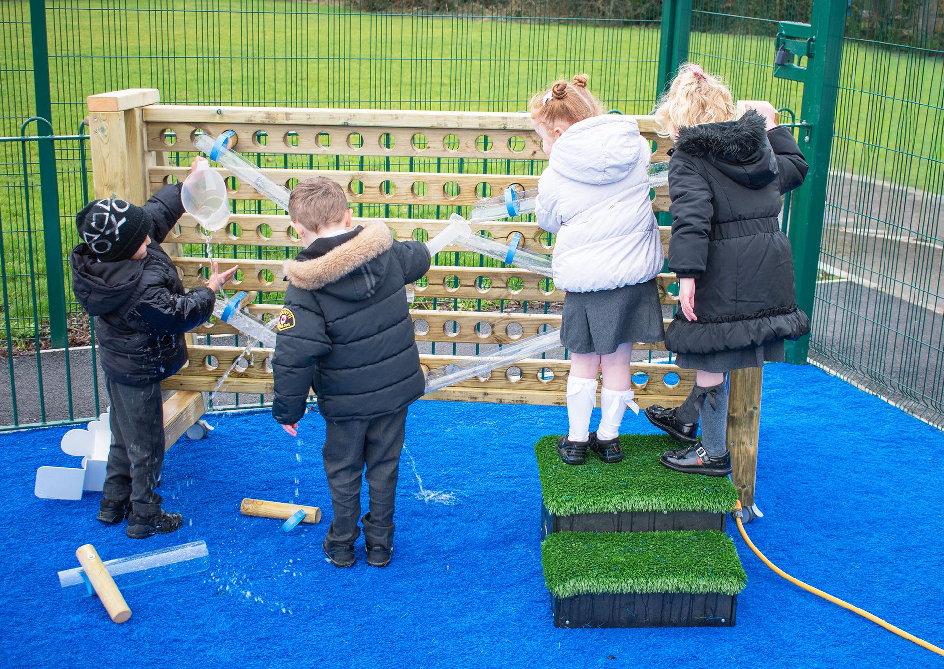 Four children playing on the movable water wall, pouring water into the water channels