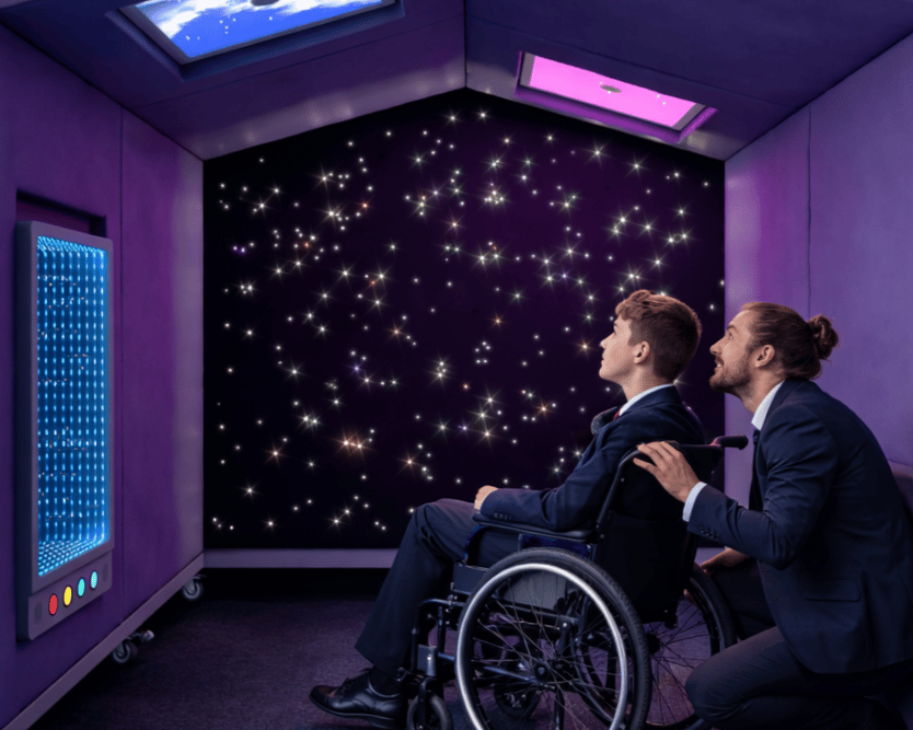 A student and a teacher are inside the Sensory Nook Shelter, as they both look at the lights.