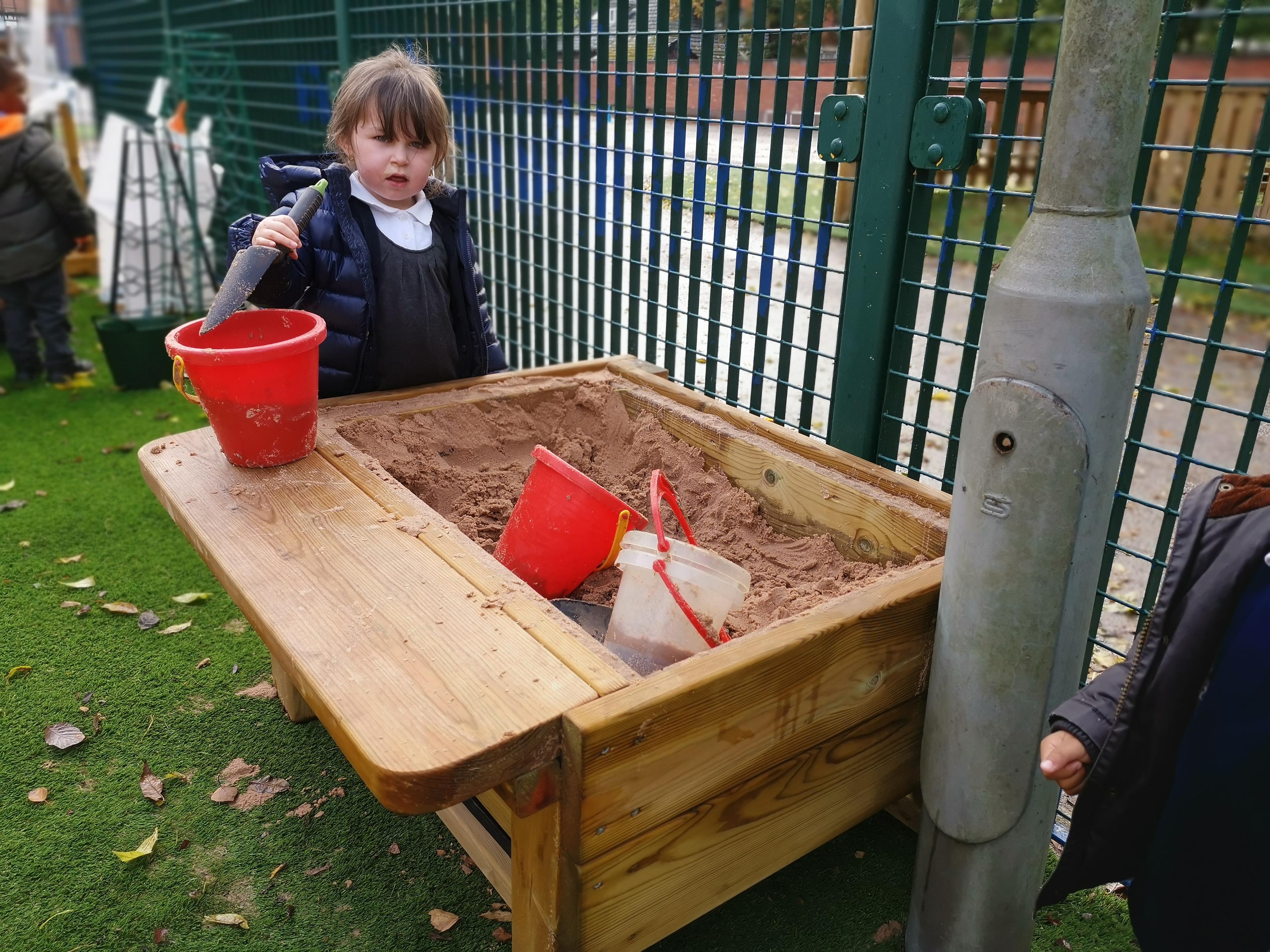 A young girl with a bucket, digging in the Pentagon Play Sand Table