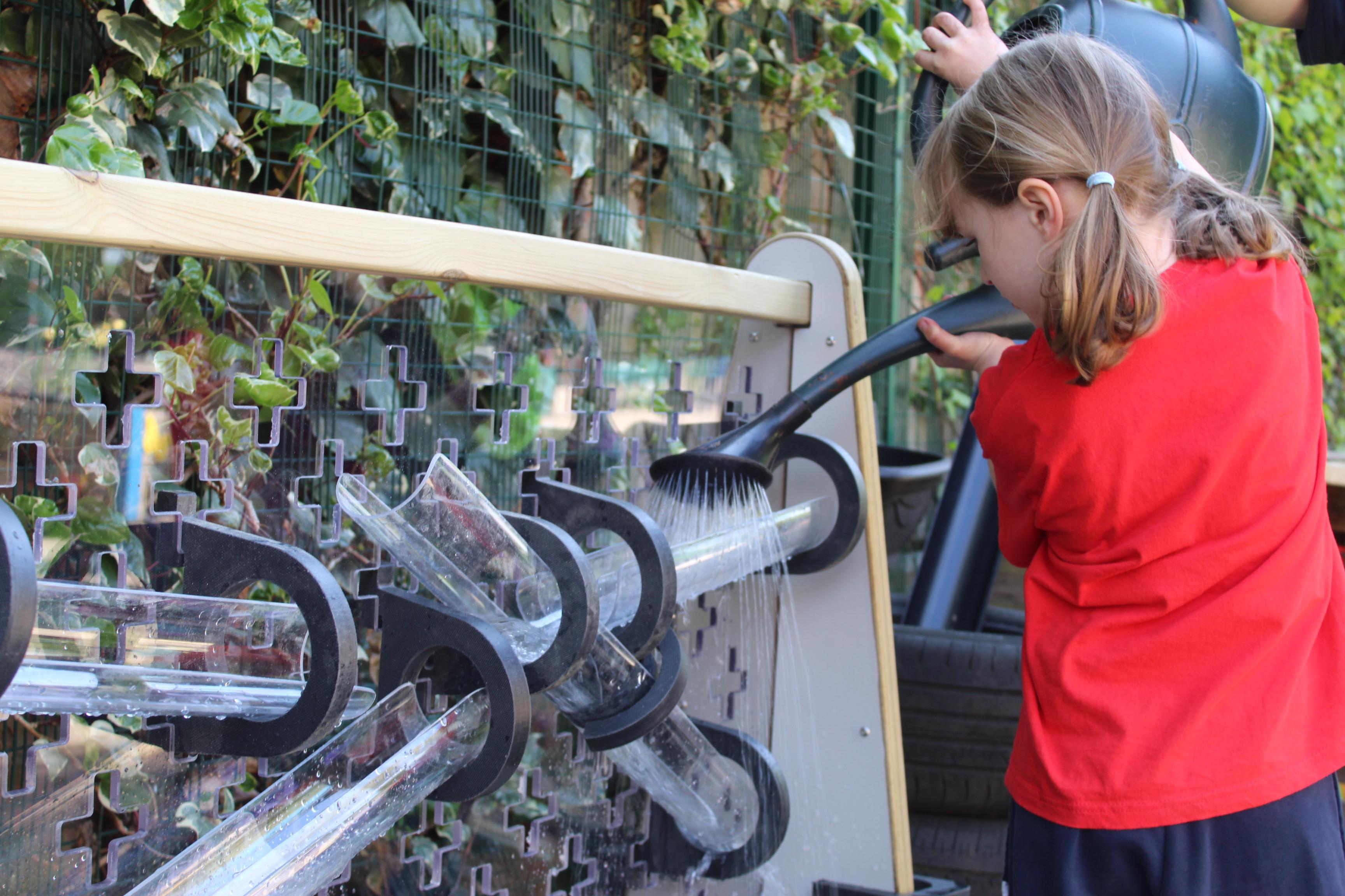 A girl pouring water into a channel on the water wall, which is part of the Inventor Messy Play Package