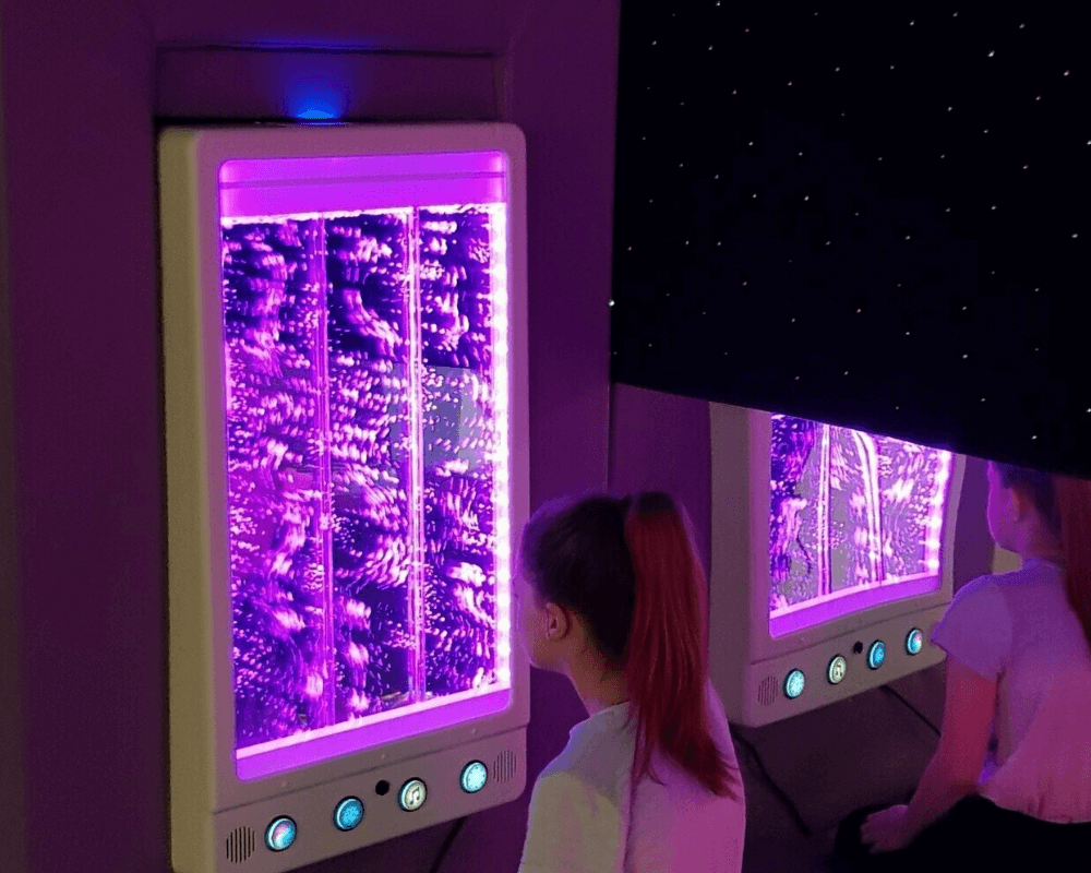 A deluxe bubble wall is installed on the wall of a sensory room, and a young girl is watching the purple bubbles