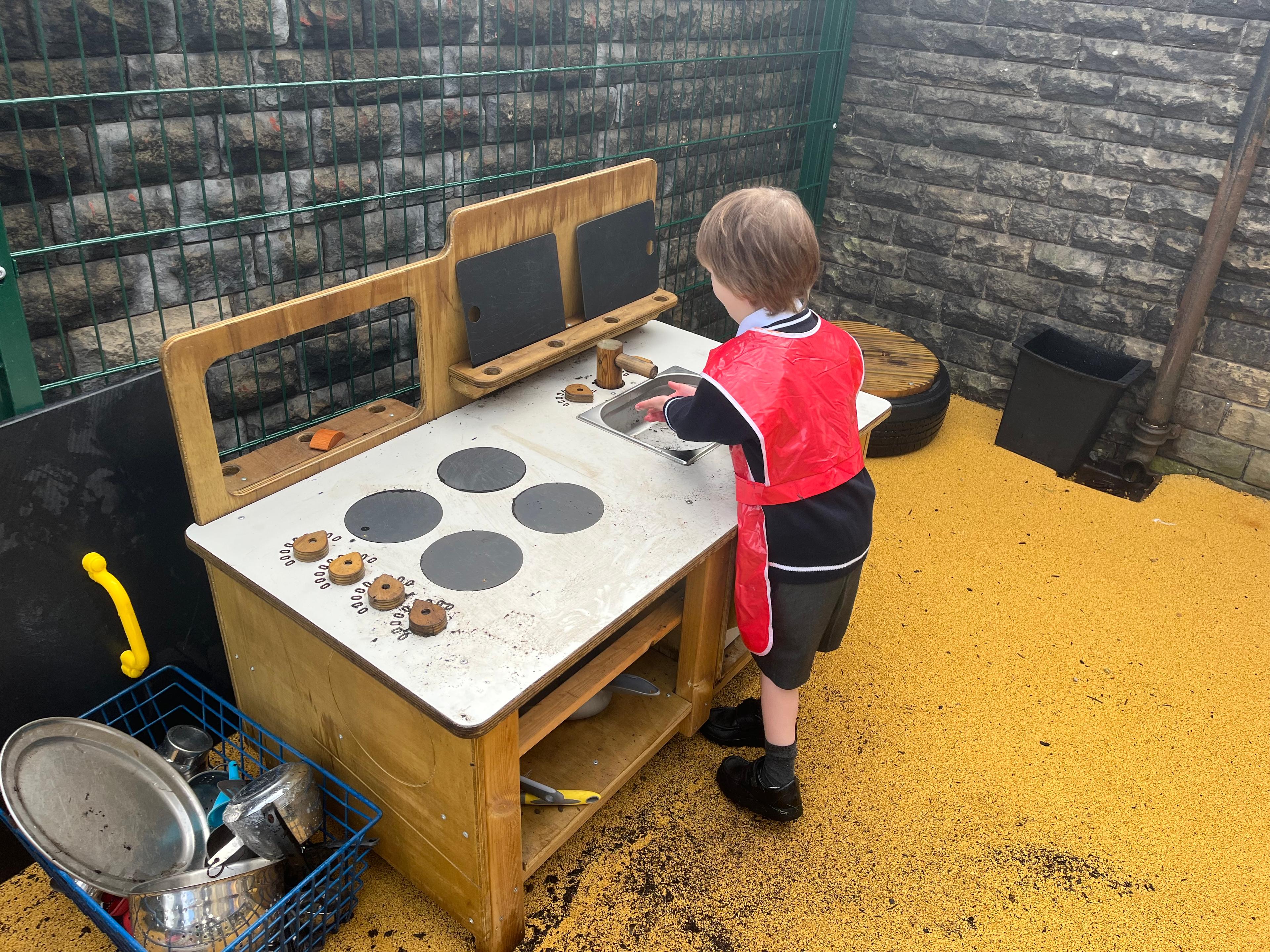 A child  playing with the mud kitchen with sink that makes up part of the Pioneer Messy Play Package