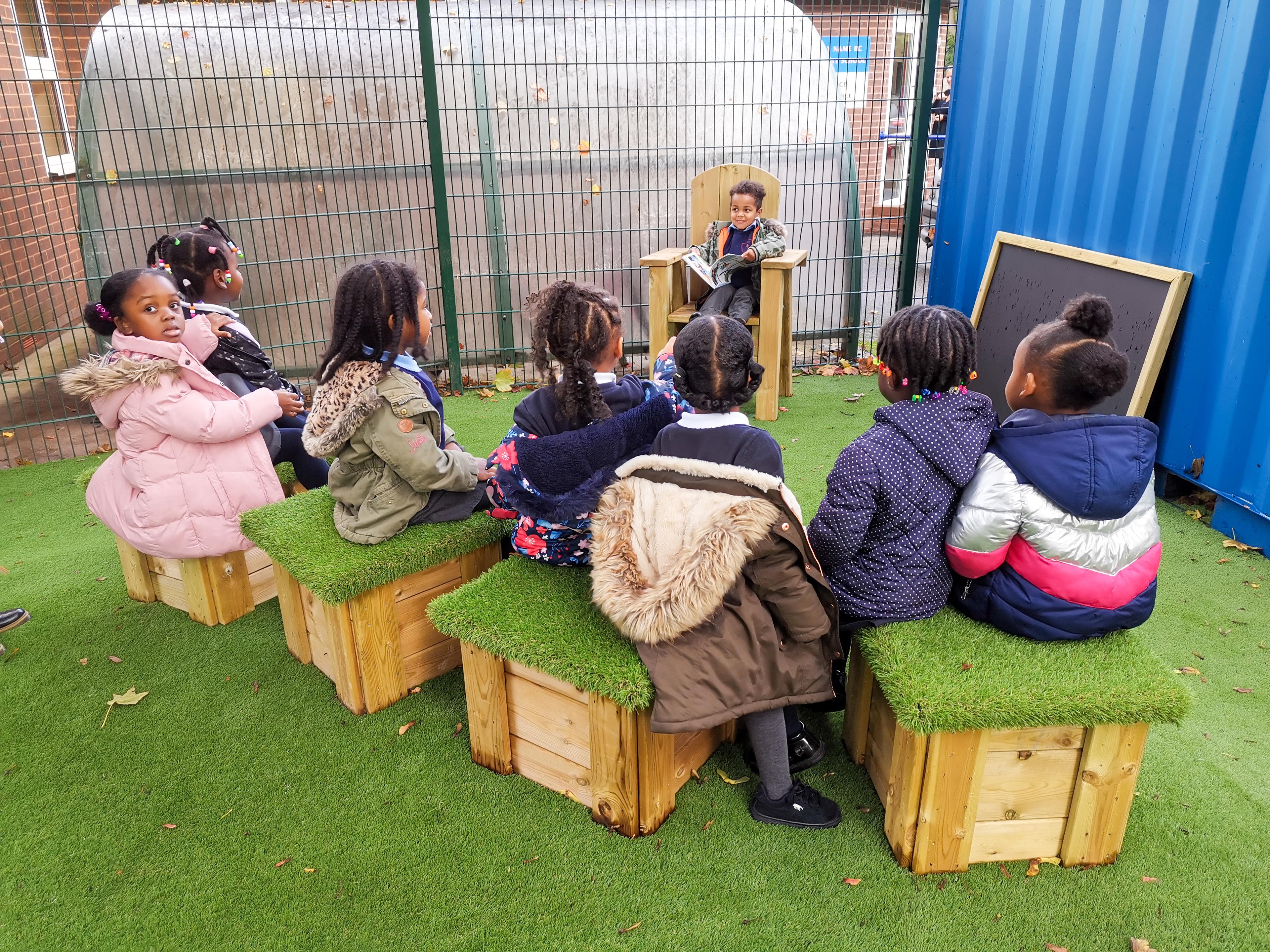 A group of children on grass topped seats listening to a story
