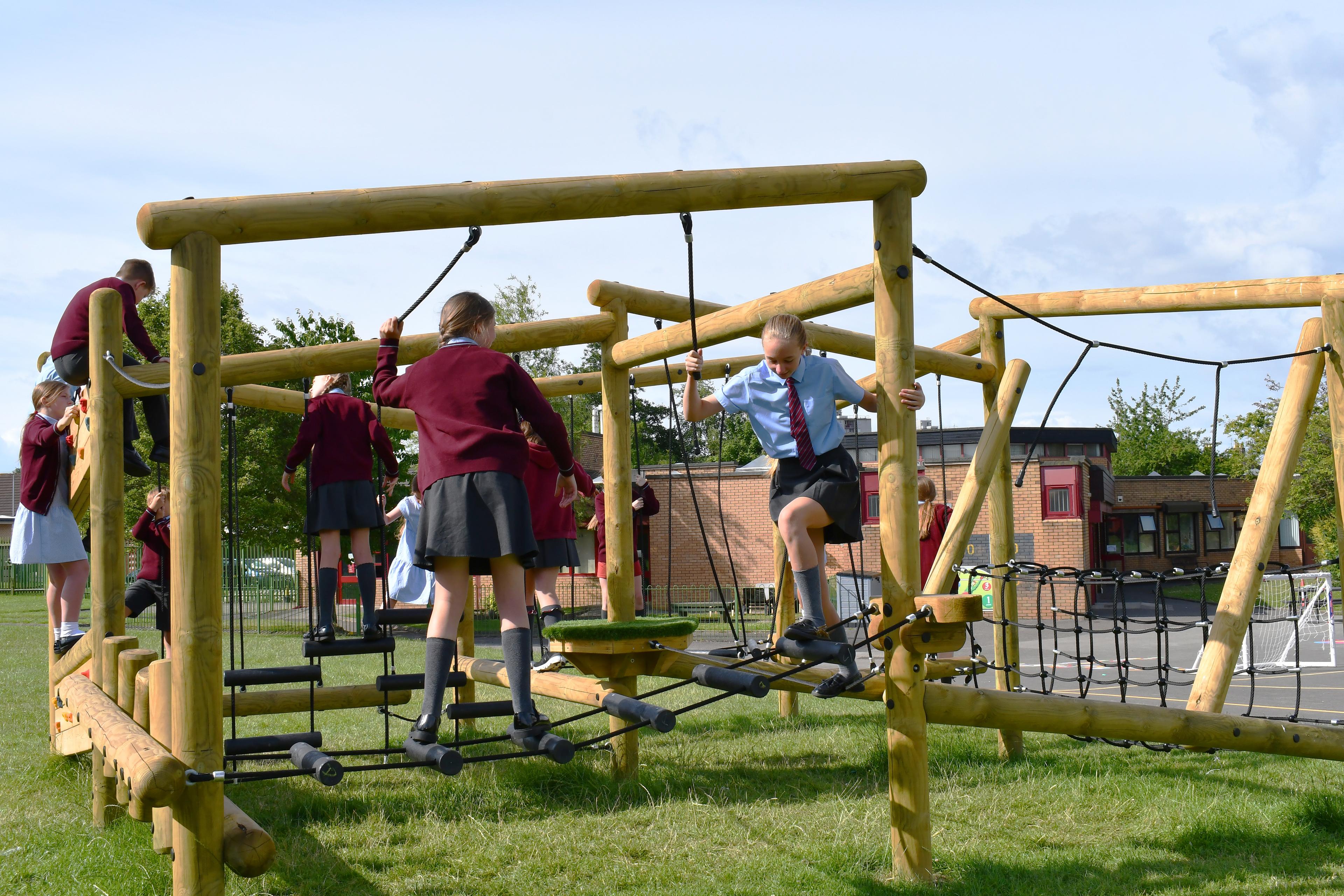 Children walking along a rope and log bridge on their school climbing frame