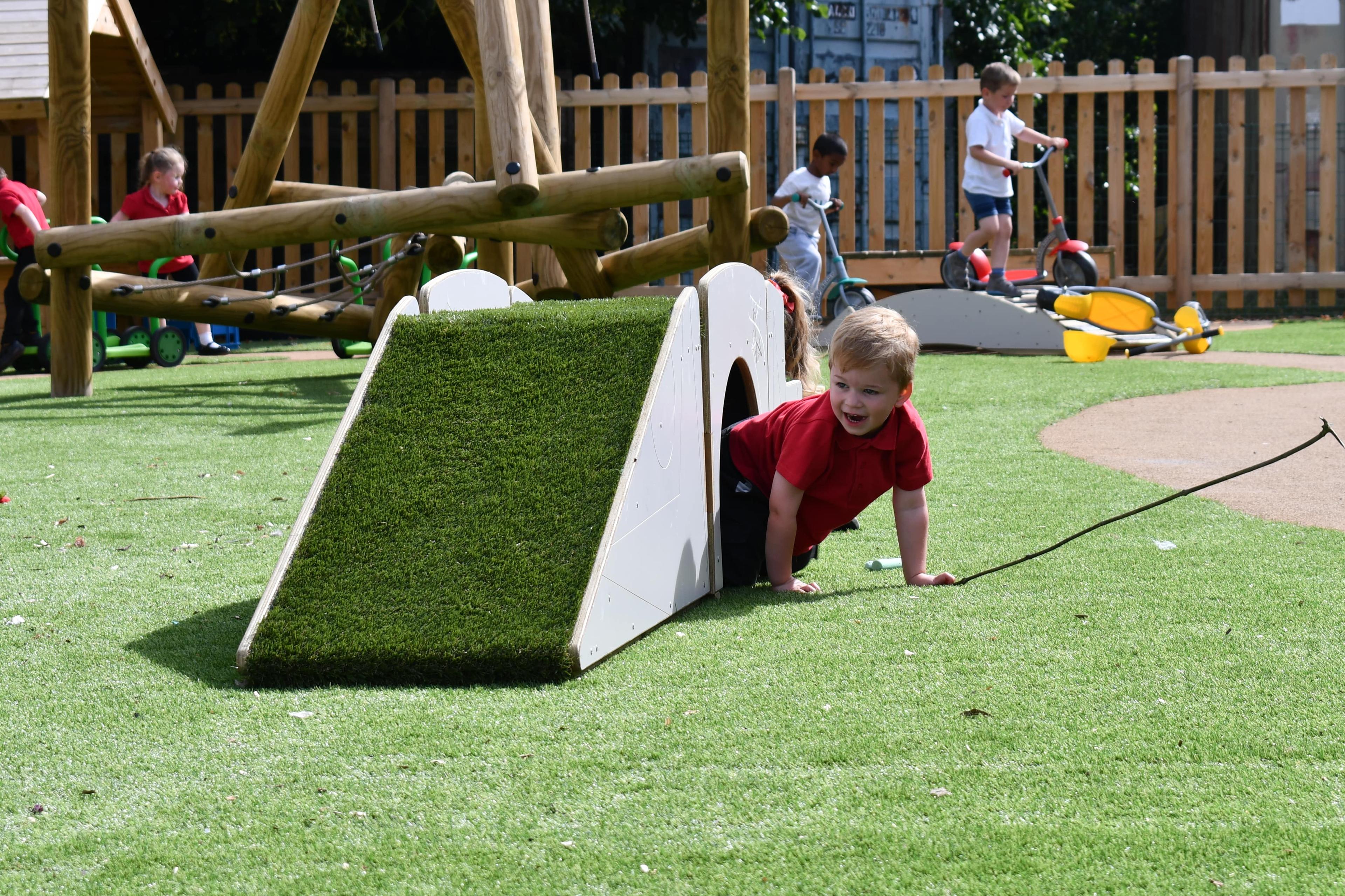 A child is crawling beneath the Up and Under set, poking their body out through the tunnel.