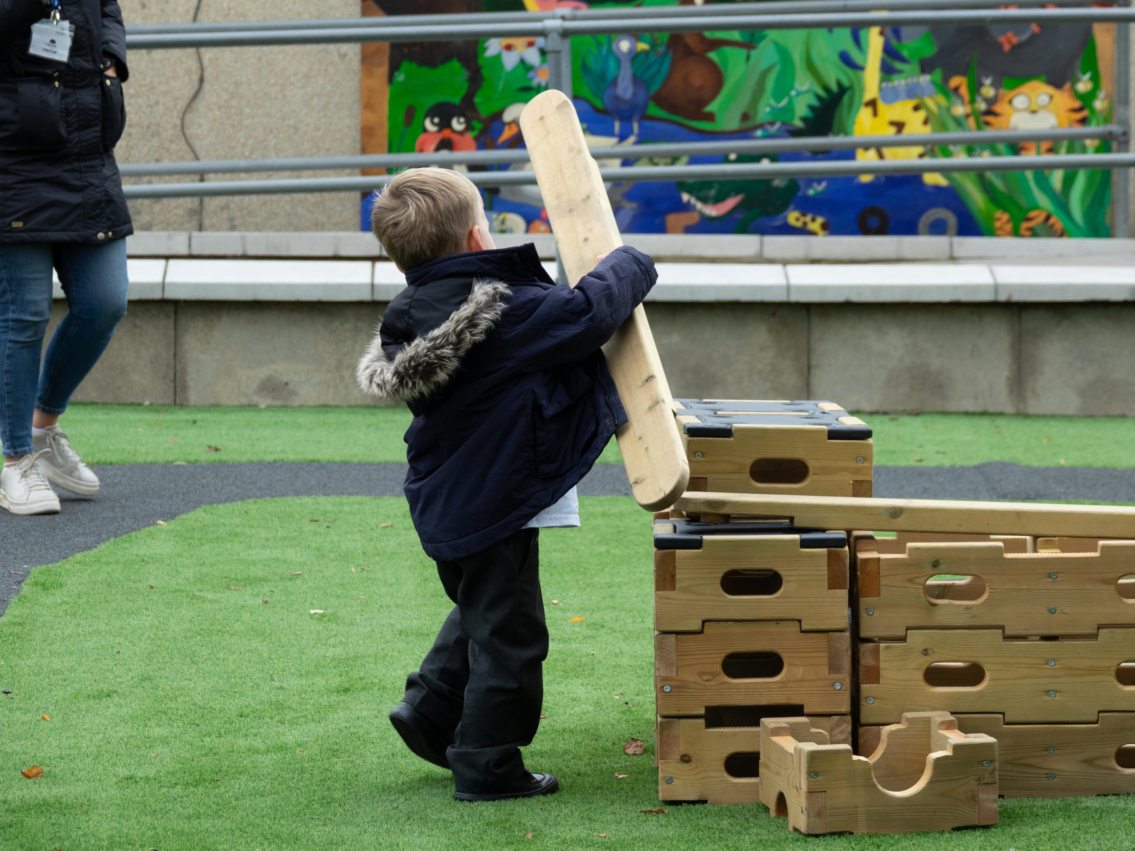 A young boy lifting up a play builder plank to place on top of a tower he has made out of play builder blocks.