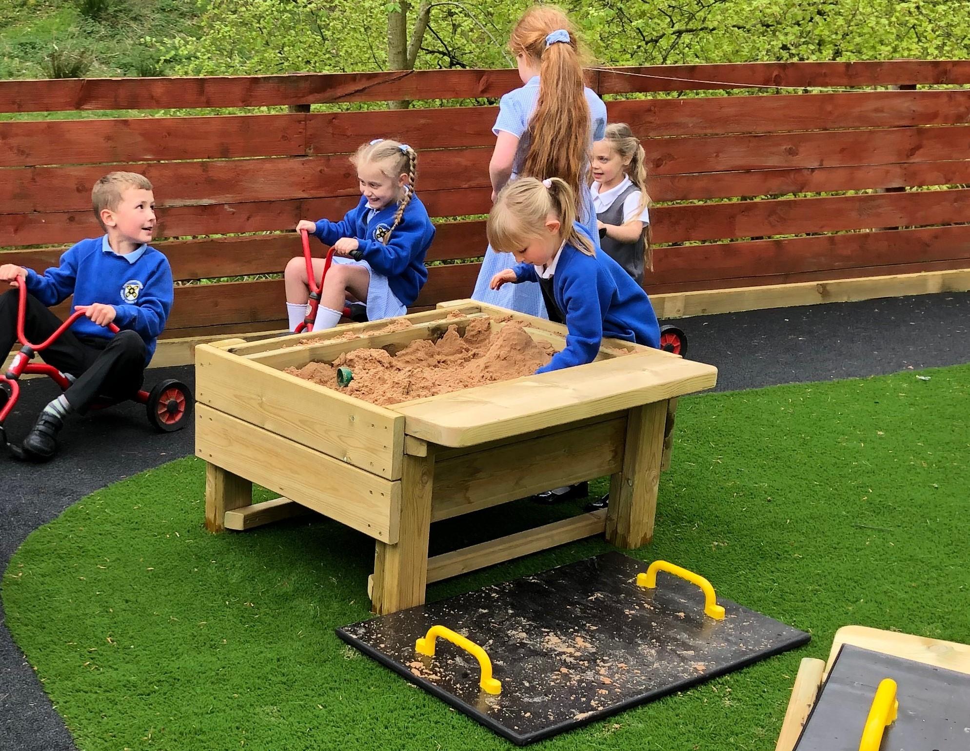 A group of children gatjered around  the Pentagon Play Sand Table