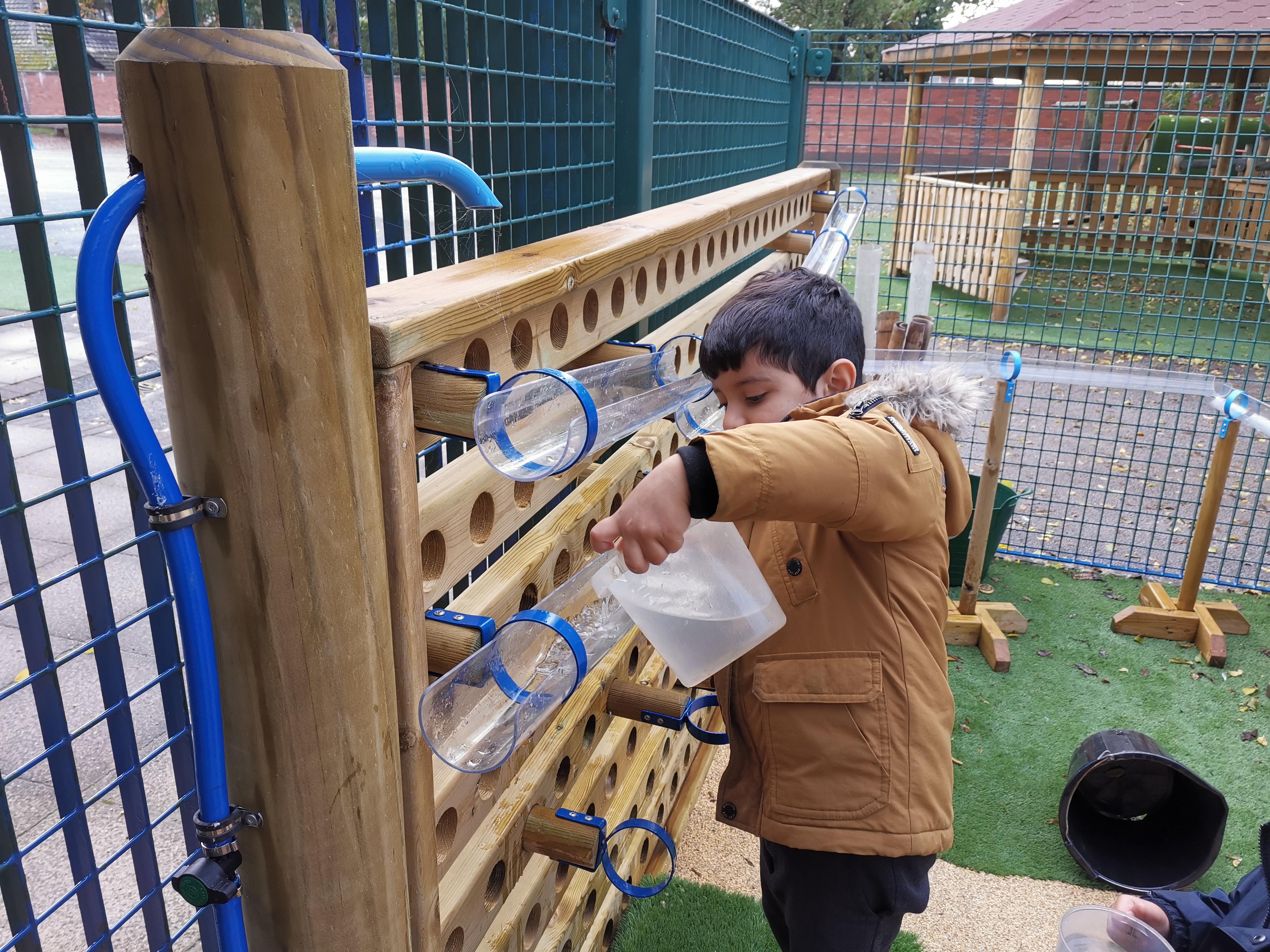 A young boy pouring water into the water wall part of the Water Wall with Water Play Package