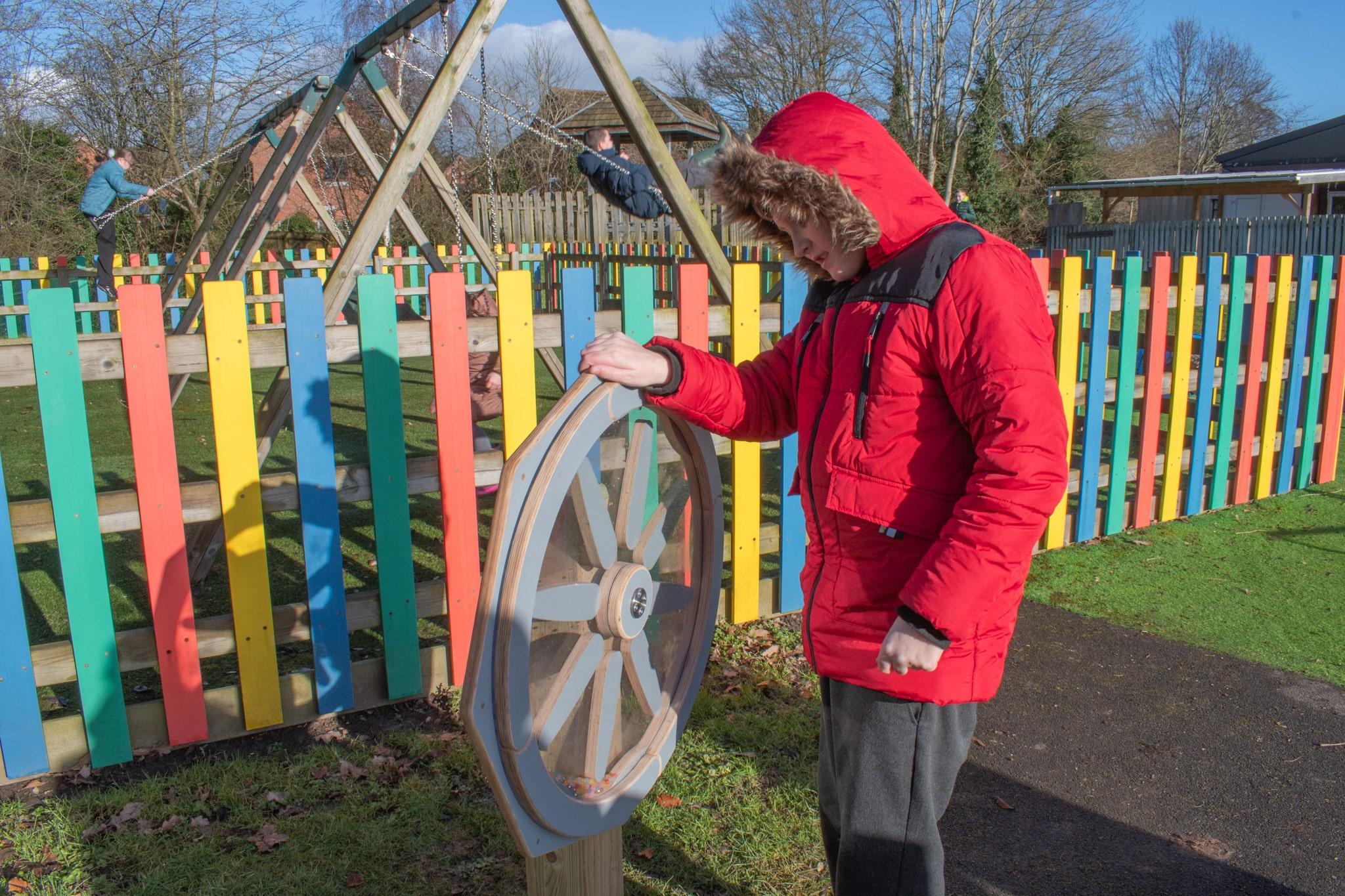 A boy in a red coat has one hand on the Sound Sensory Spinner and is spinning it.