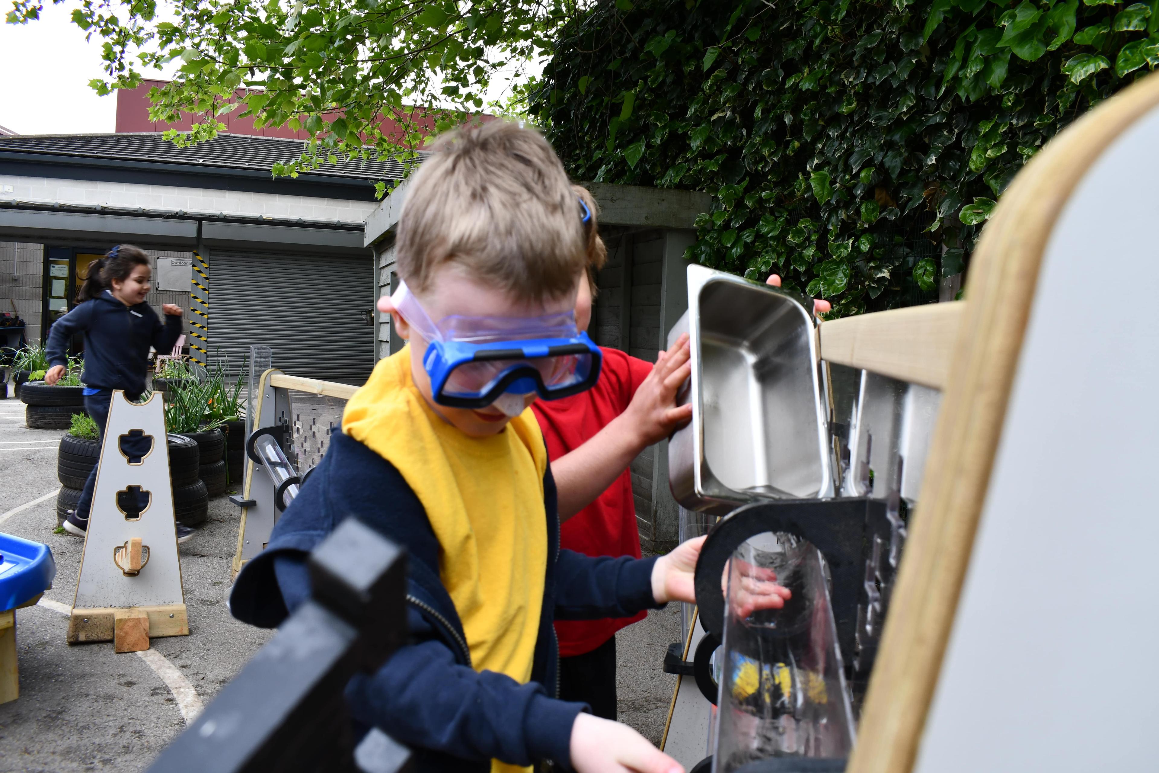 A little boy is wearing goggles as he pours water into the water wall pipes.