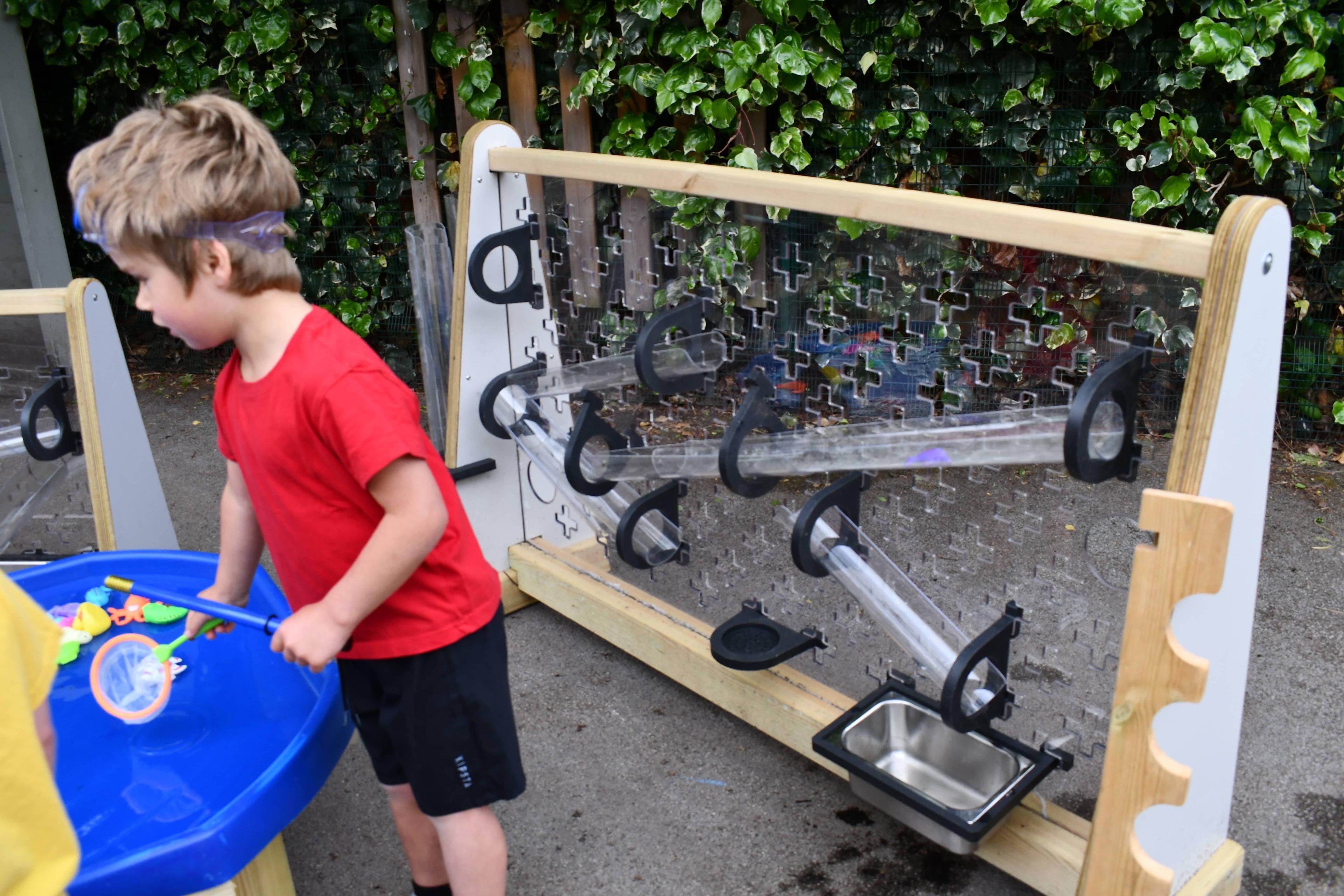 A freestanding water wall is behind a little boy who is playing with water in a tuff spot table.