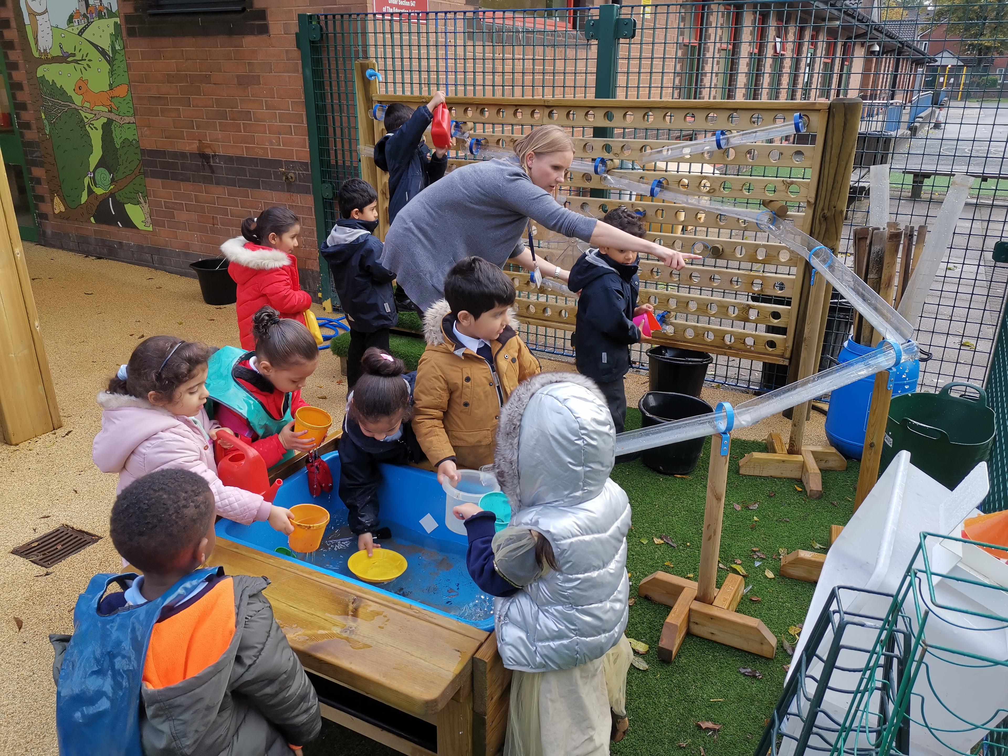 EYFS children and a teacher interacting with the Water Wall with Water Play Package