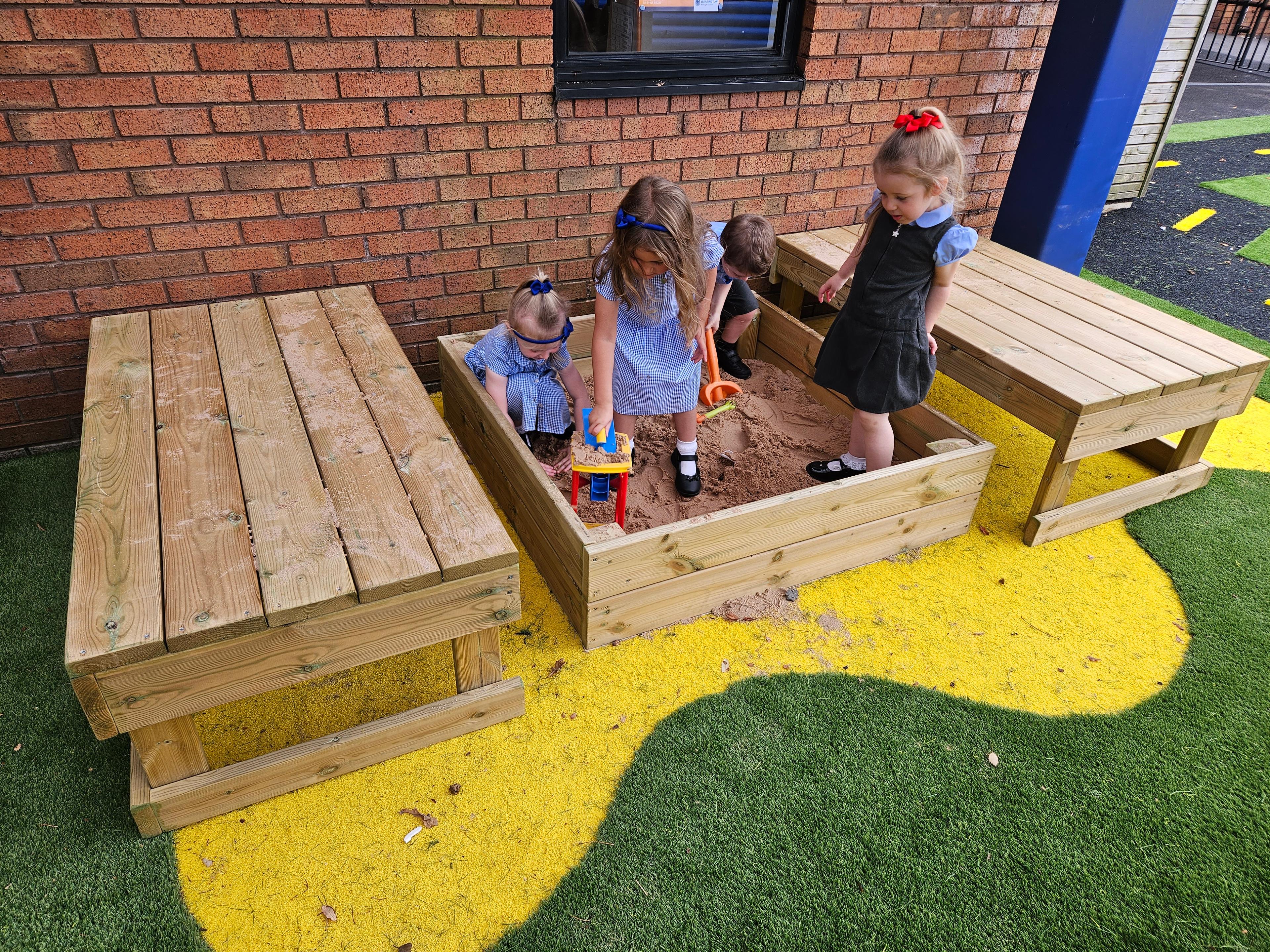 Four children are playing inside the small covered sand box as they dig and build.