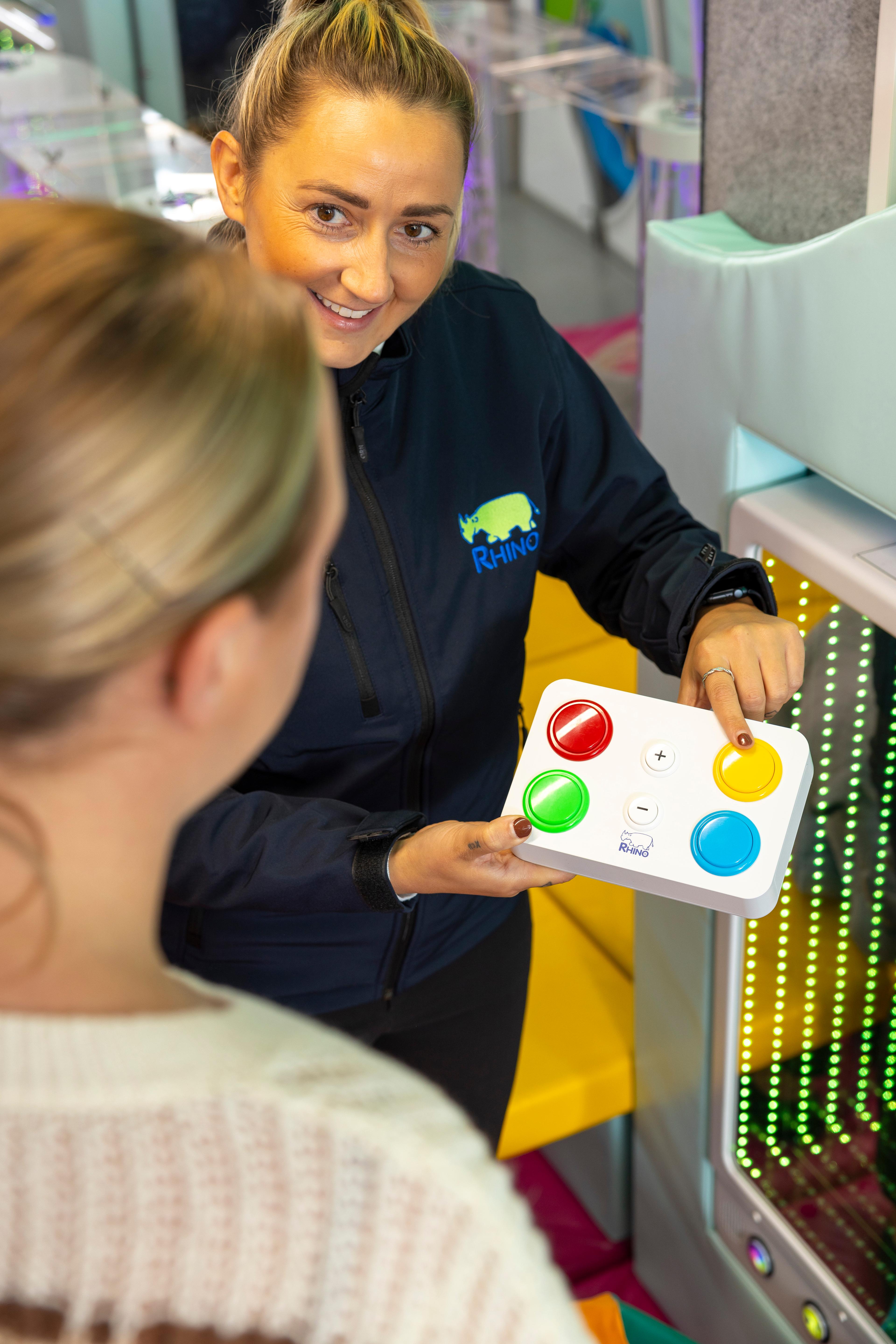 A woman holding a white remote control with four large buttons that are red, yellow, green and blue.