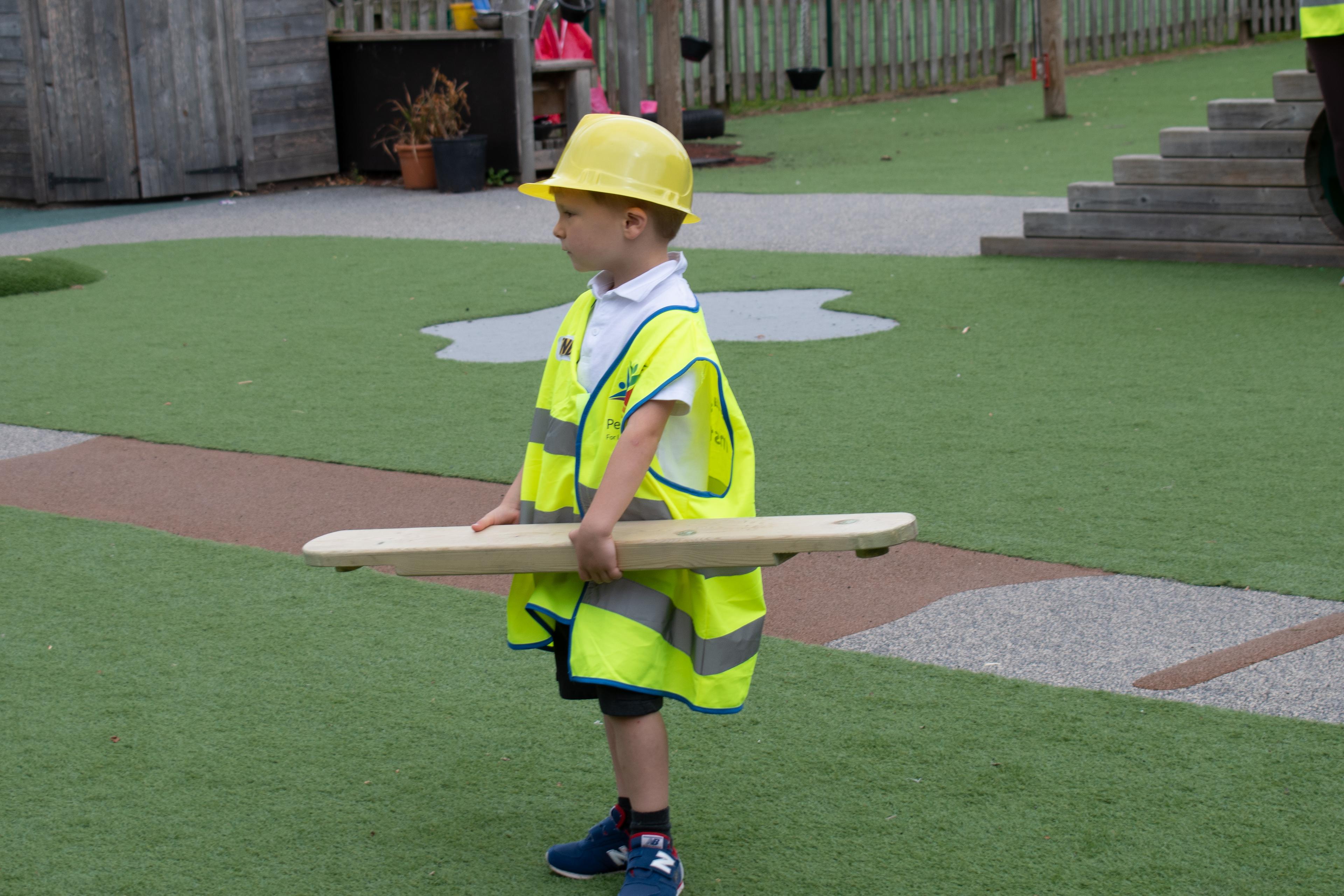 A young boy dressed as a builder holding a play builder plank