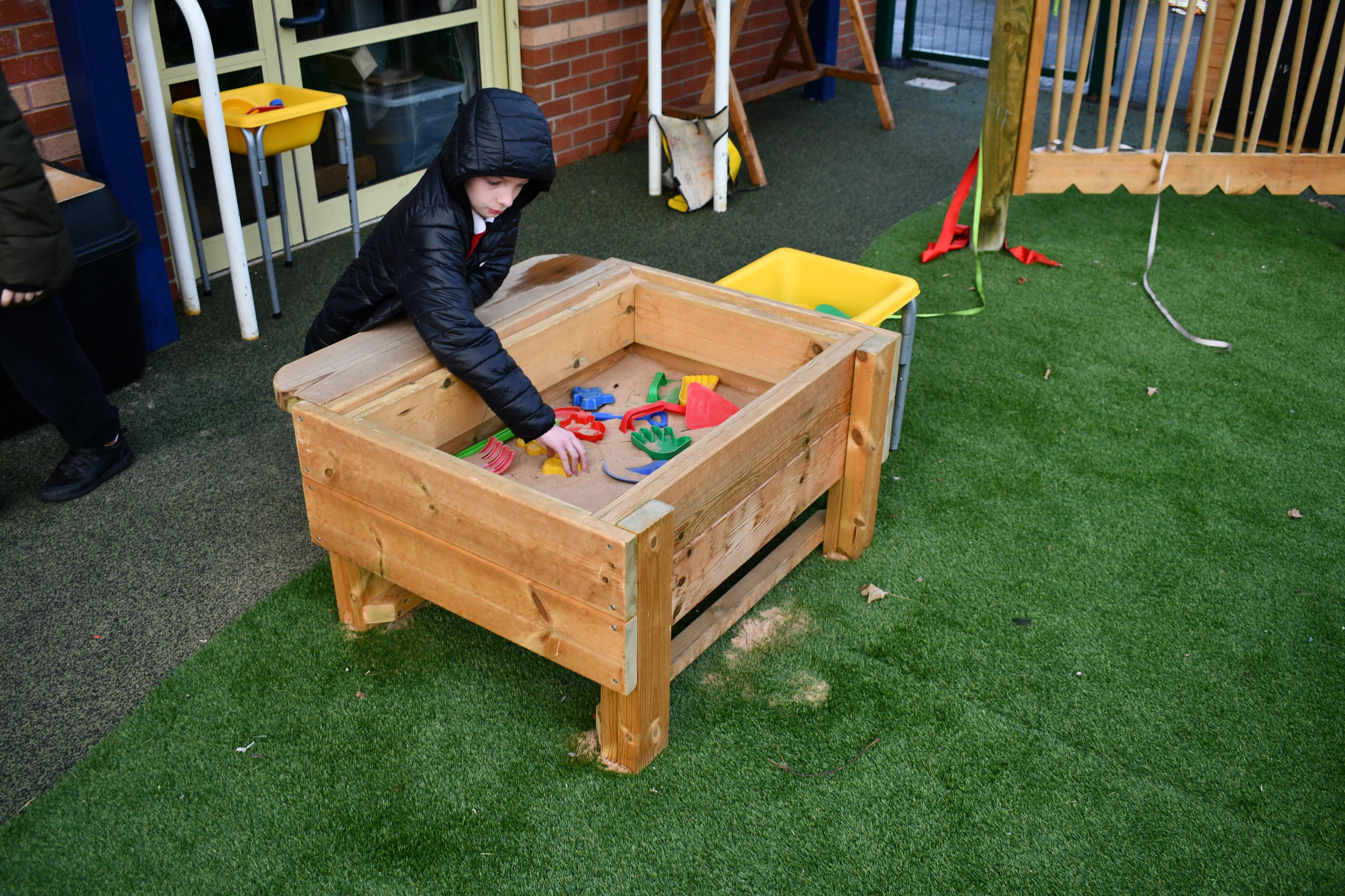 A young boy with a digging in the Pentagon Play Sand Table with a spade