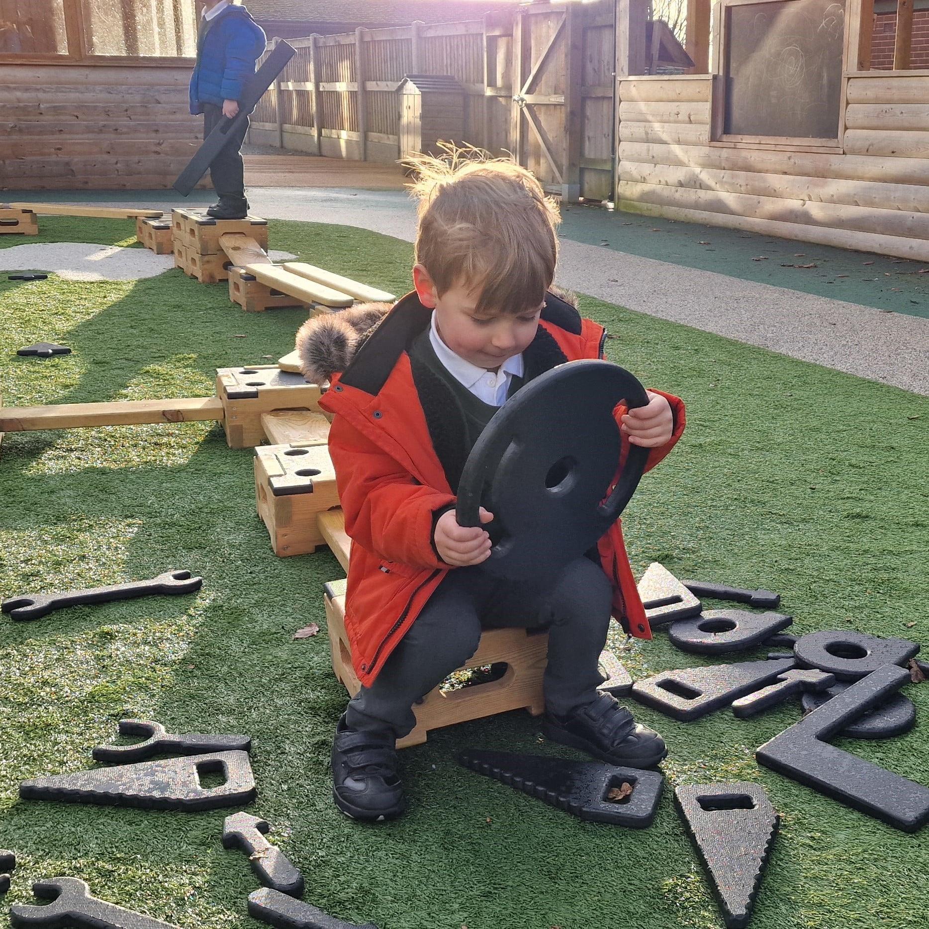 A young boy sat on the playbuilder set using the role play addtions as a car's steering wheel
