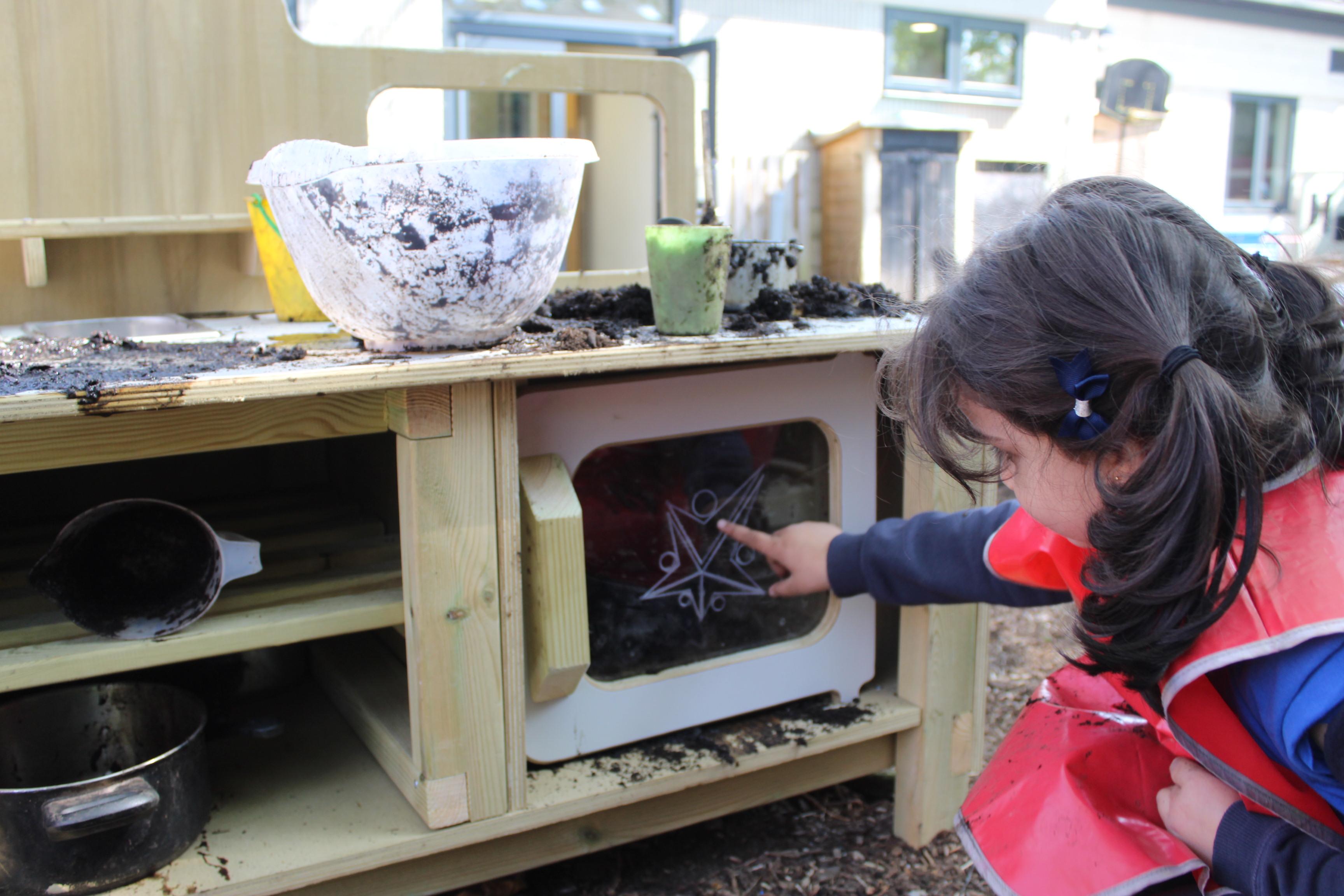 A child playing with the mud kitchen with oven that makes up part of the Pioneer Messy Play Package