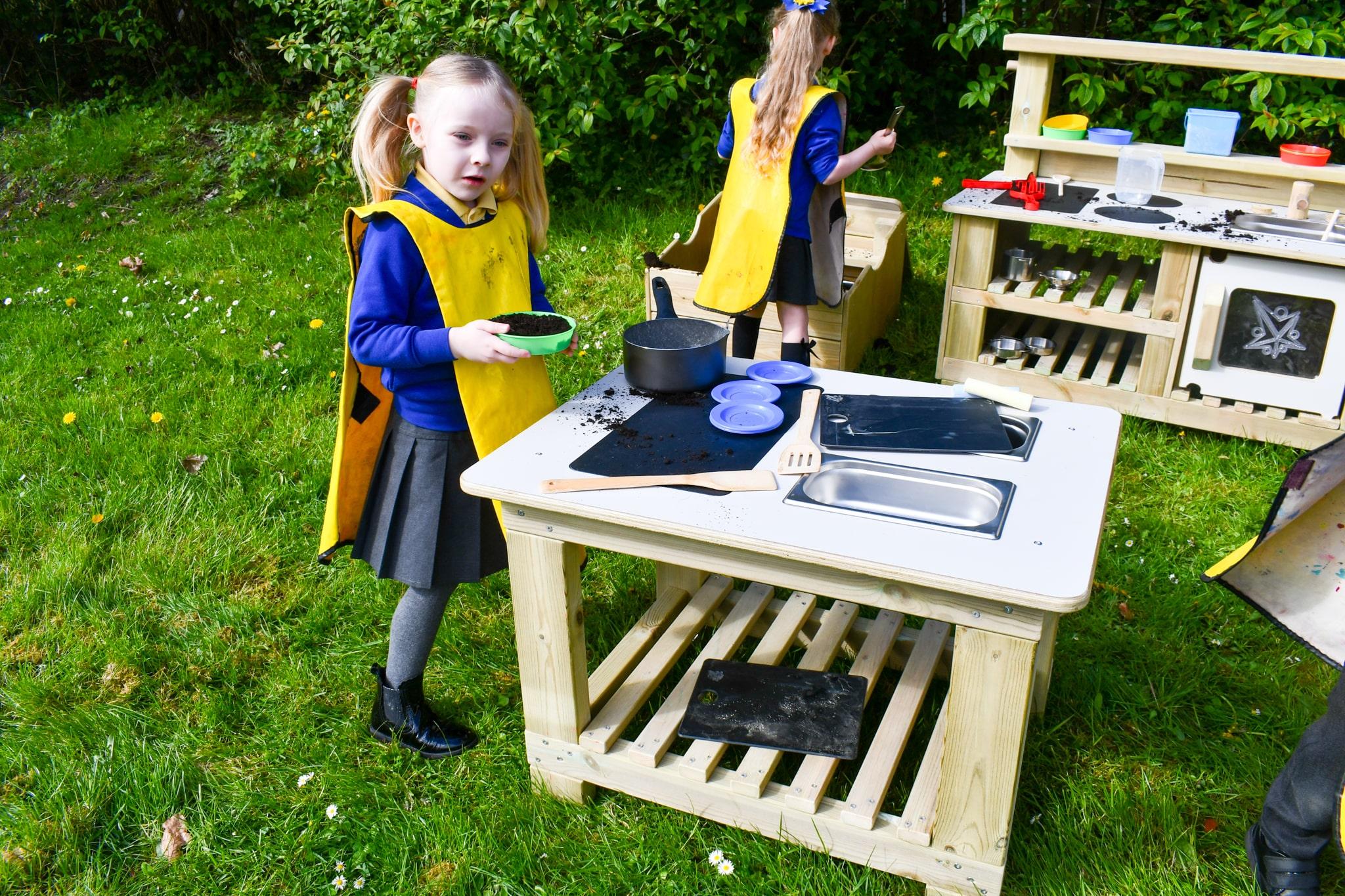 A little girl is bringing over a bowl of mud to the surface of the Mud Kitchen Island.
