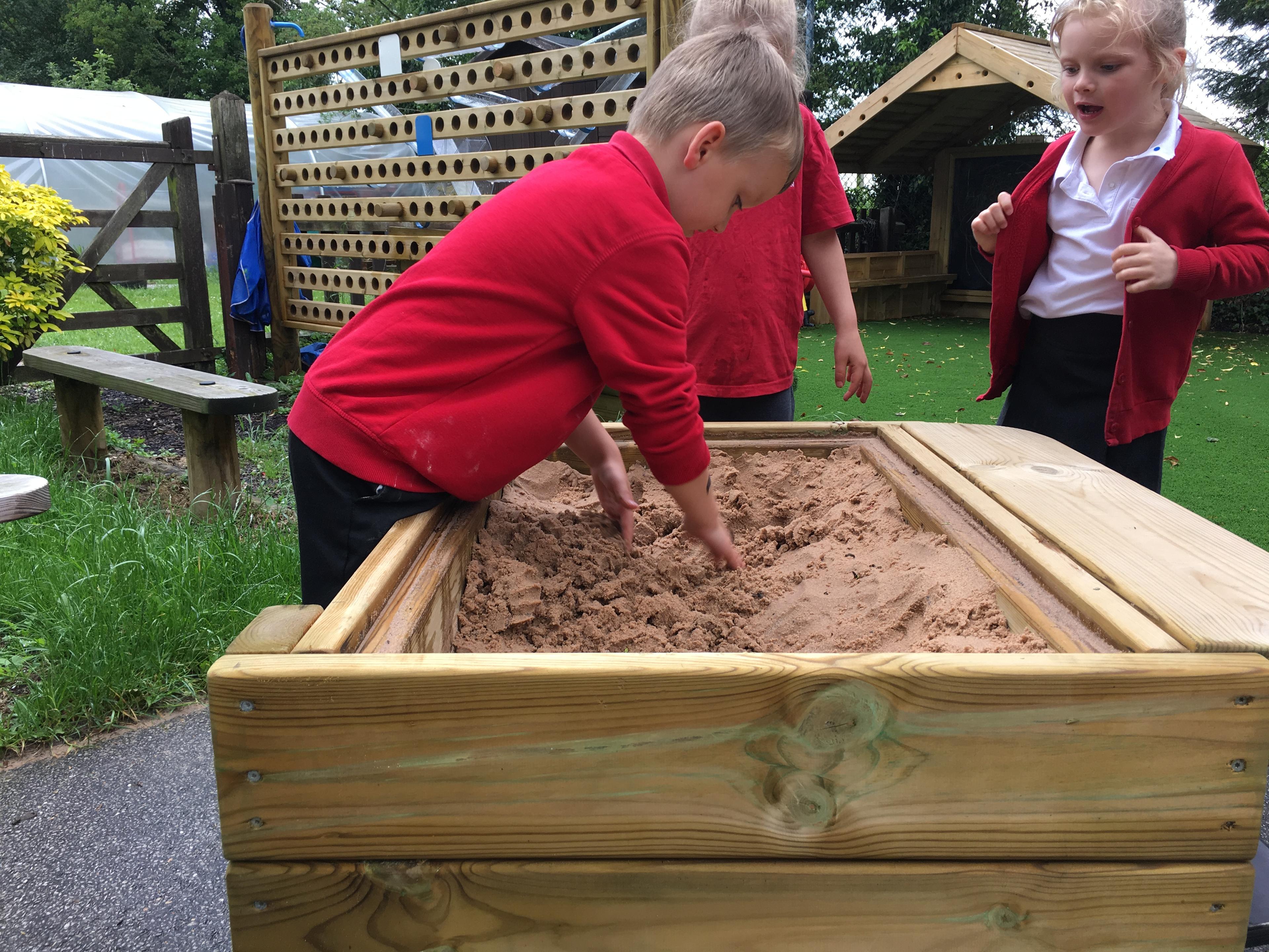 A group of children digging with their hands in the Pentagon Play Sand Table