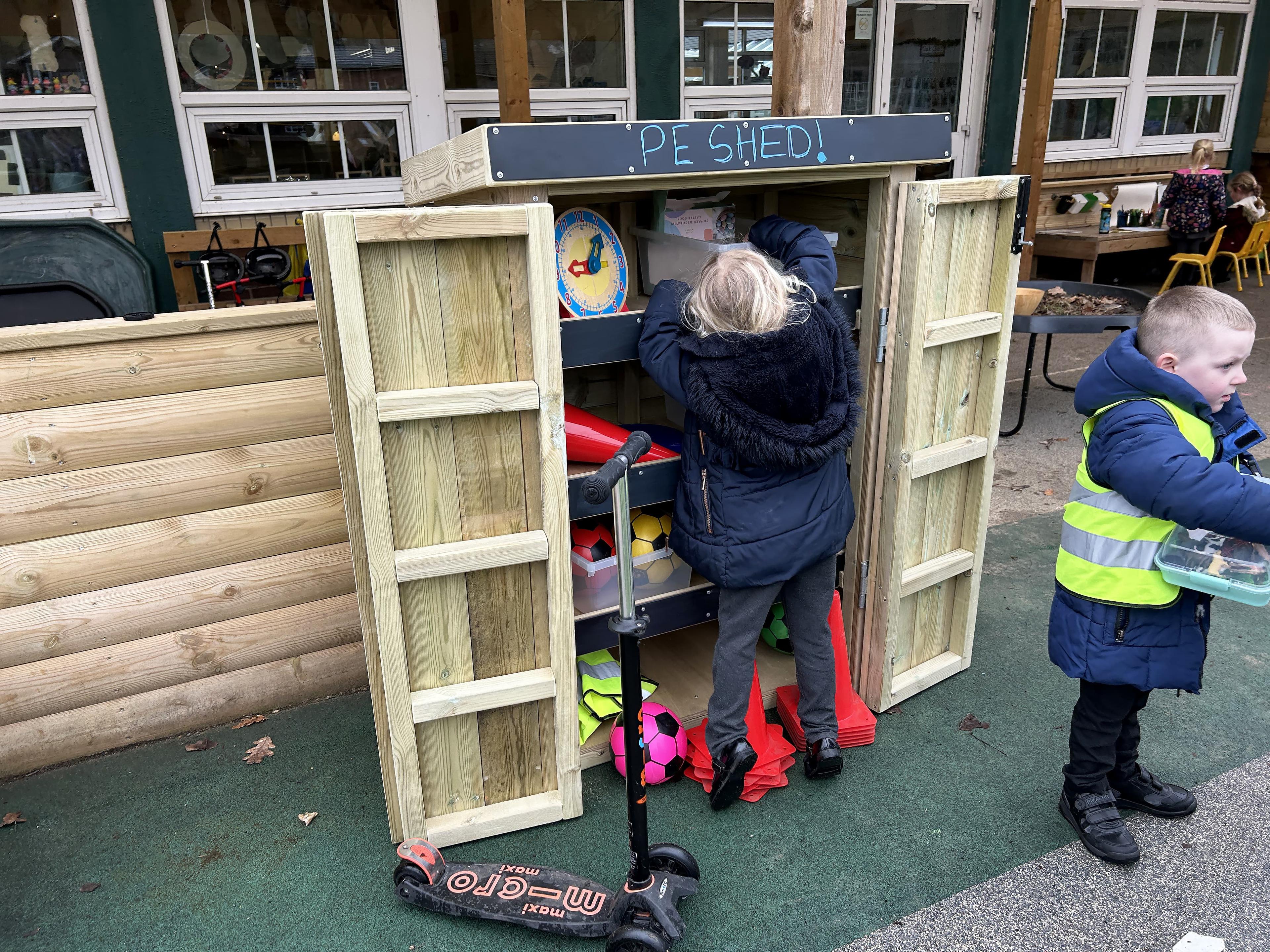 Young school girl getting resources out of a Wooden Acorn Storage Unit in a school playground