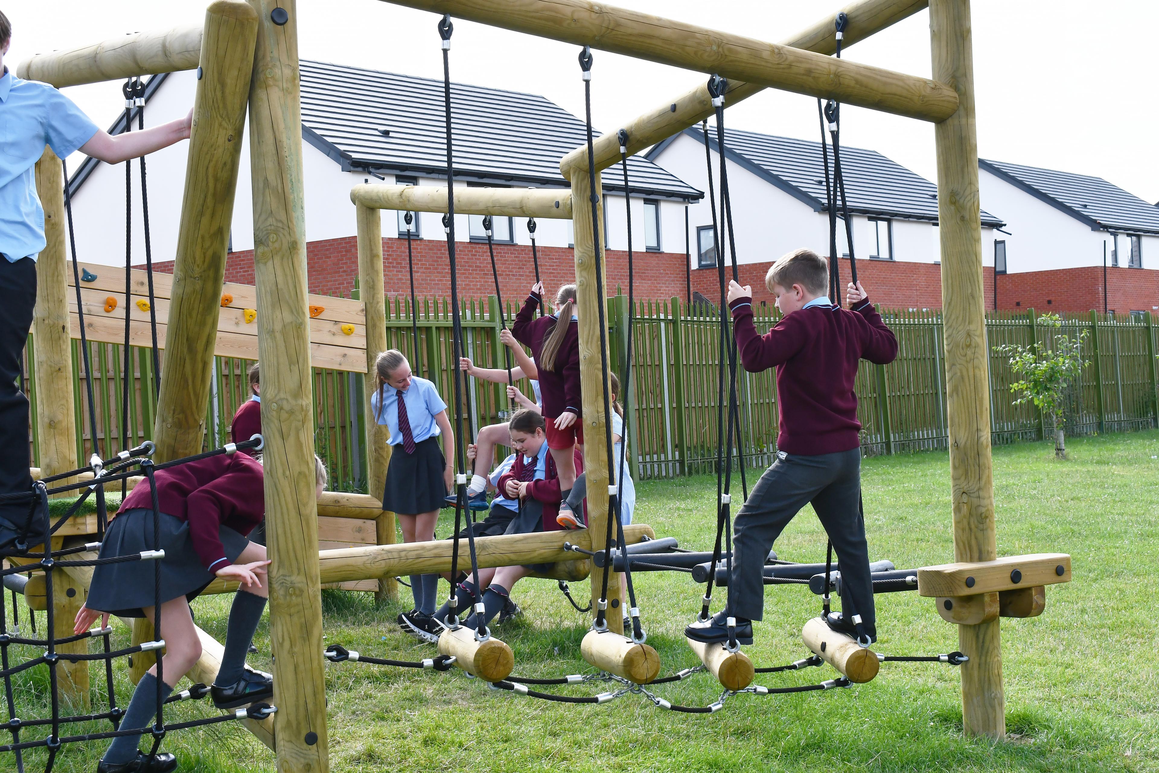 Children holding on to ropes and balancing on logs that are part of a climbing frame in their school playground