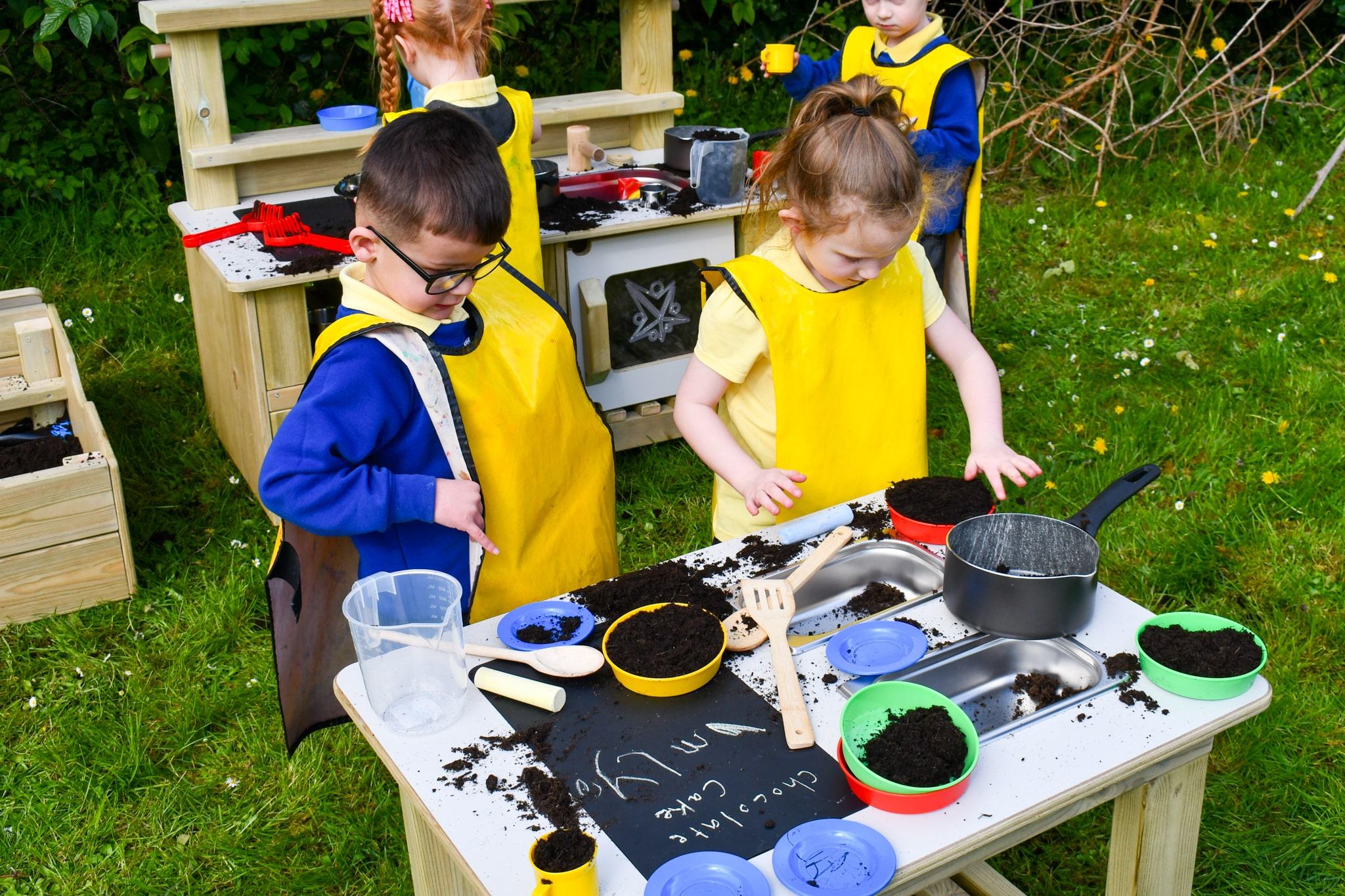 An EYFS boy and girl are using messy play resources on the Mud Kitchen Island.