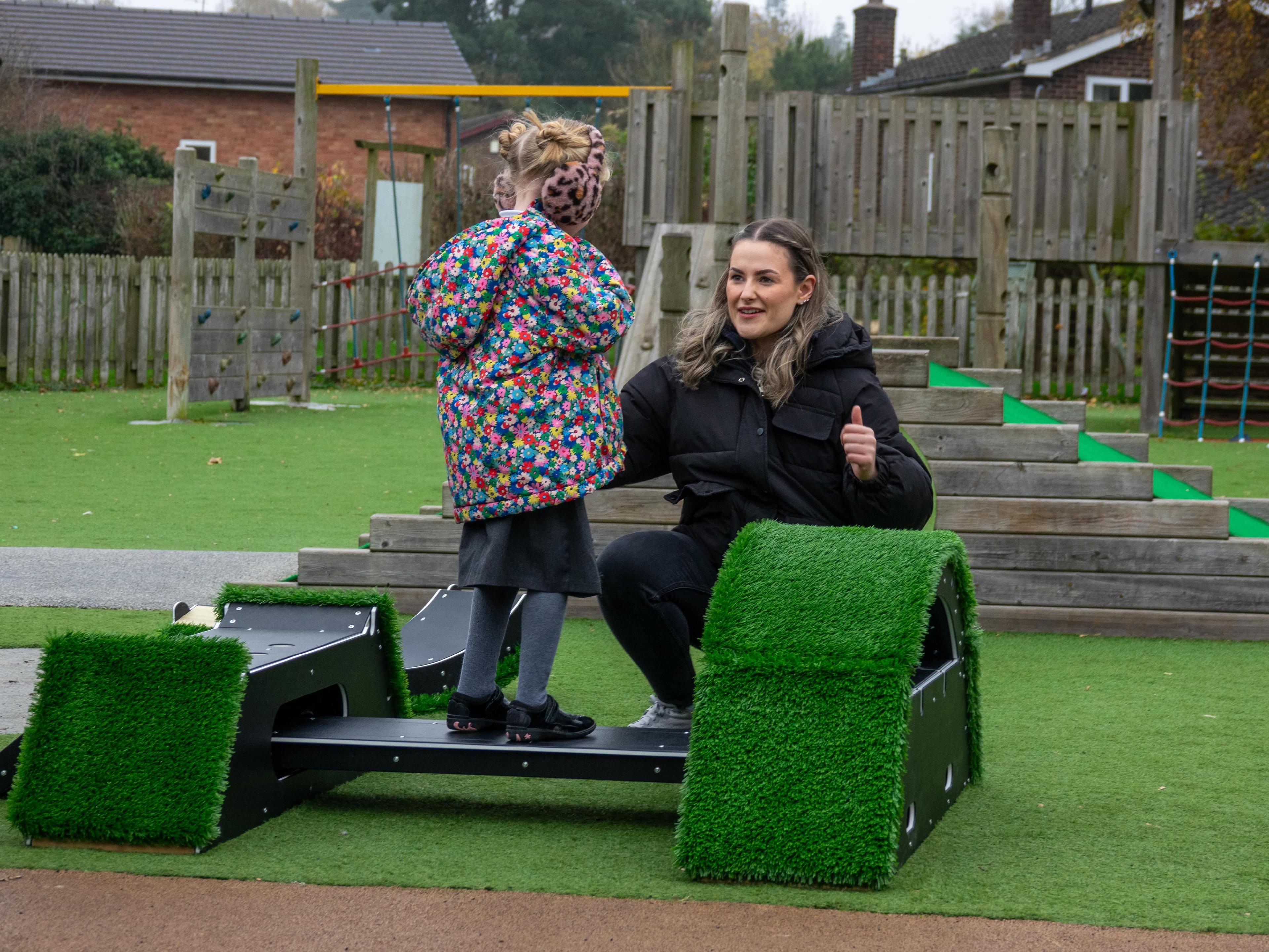 A woman is giving a thumbs up to a little girl who is stood on the wobbleboard that is attached to the Rockies.