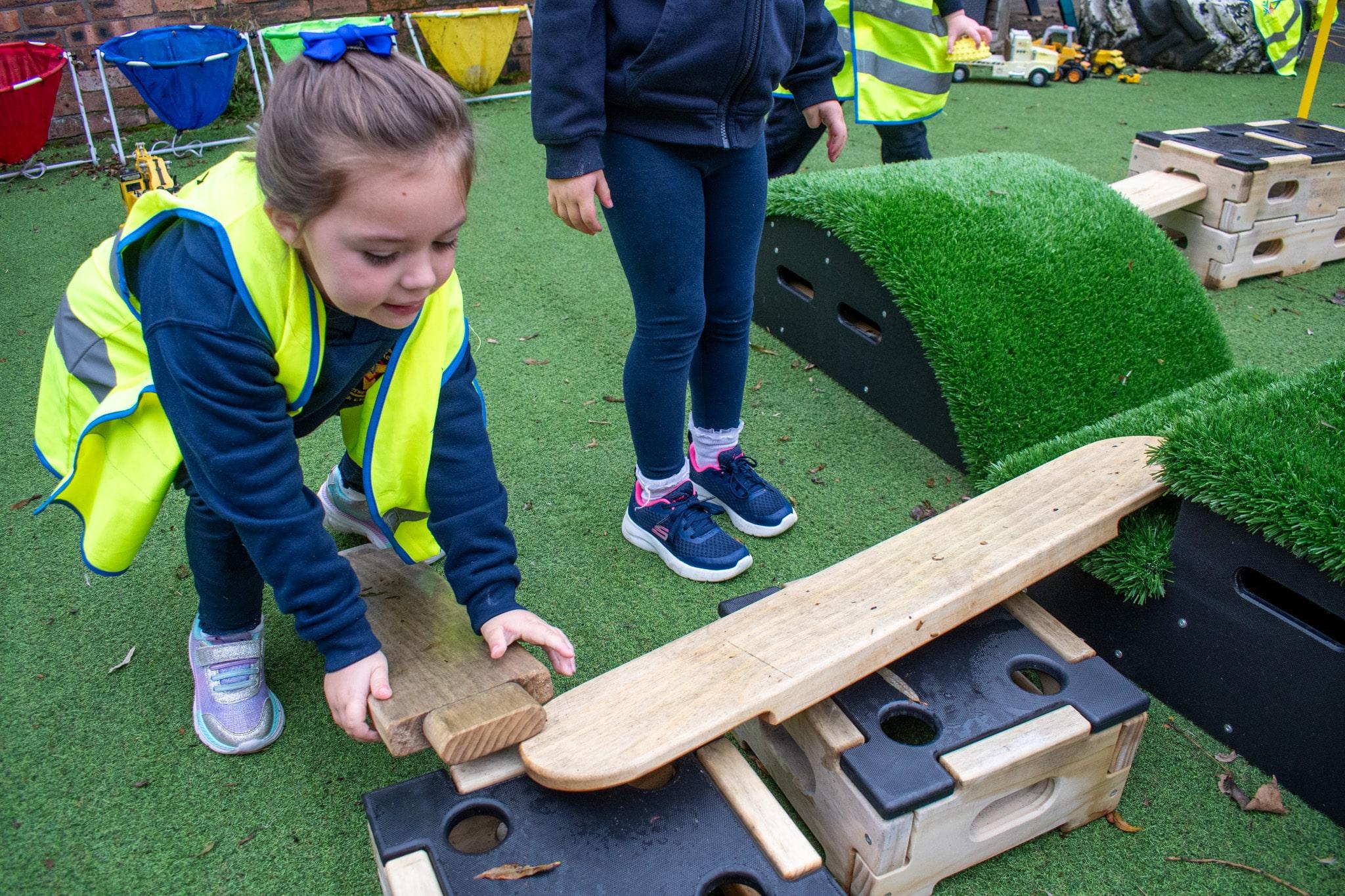 A close up of a girl attaching a wooden plank between a Get Set Go block and a Play Builder block.