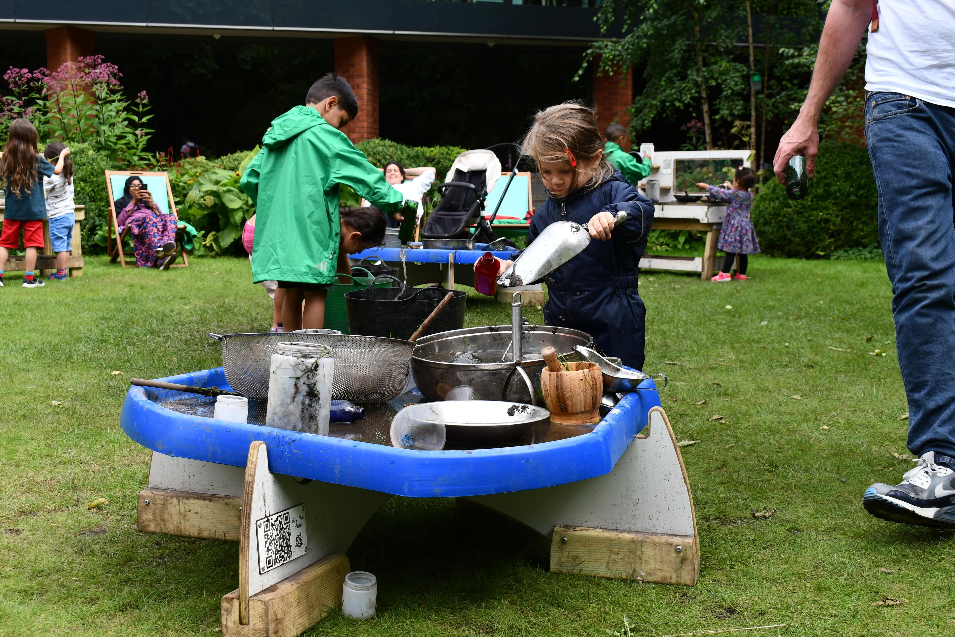 A little girl is carrying water over to a tuff spot table.