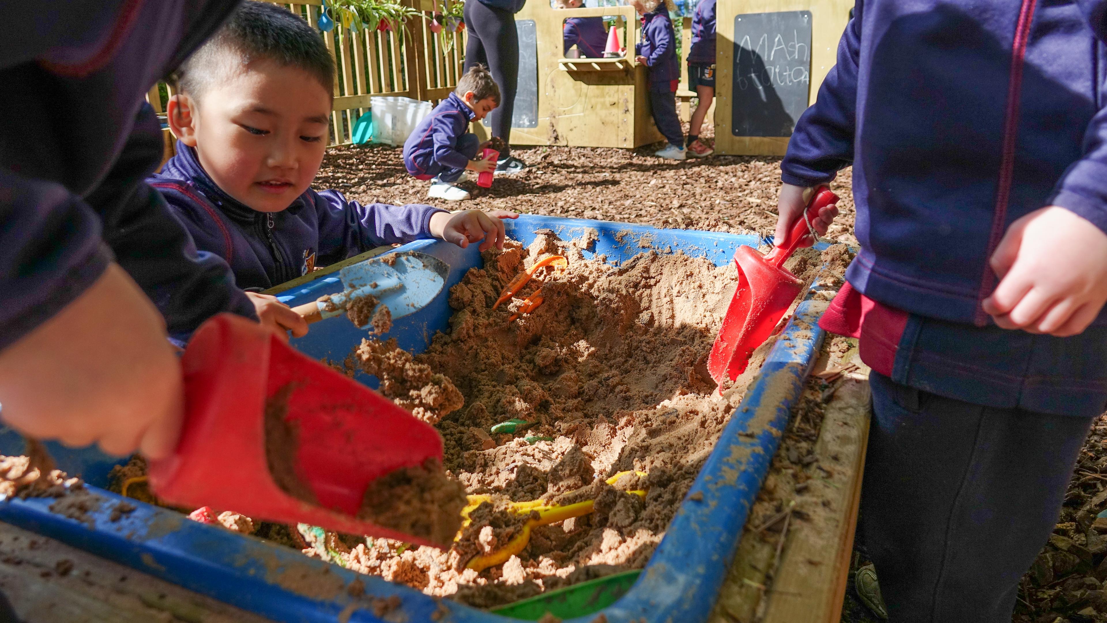 A group of children digging in the Pentagon Play sand table on wheels