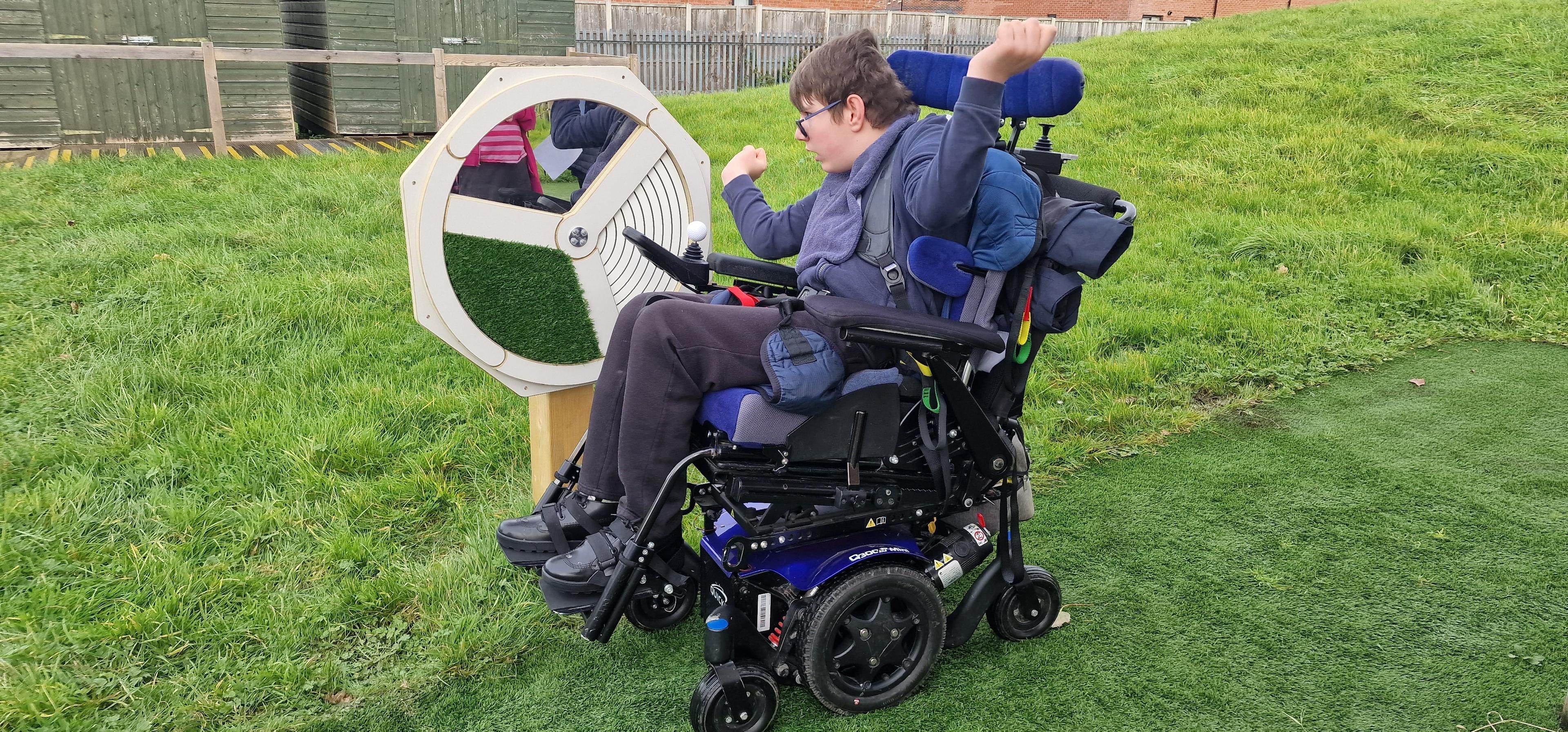 A boy in a wheelchair is looking at his reflection in the Touch Sensory Spinner.