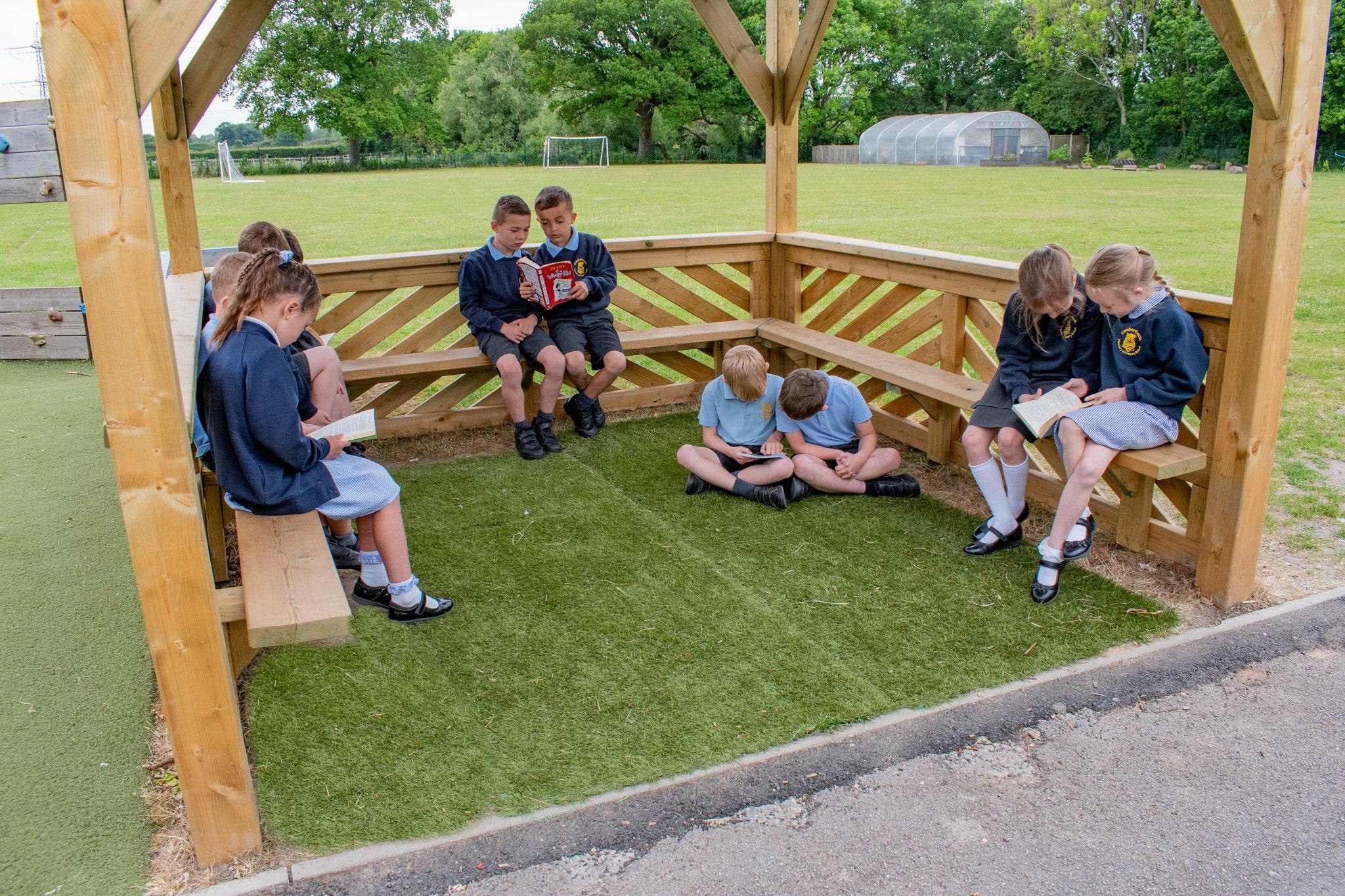 A group of children are sat inside the 3m square gazebo as they are reading a variety of different books.