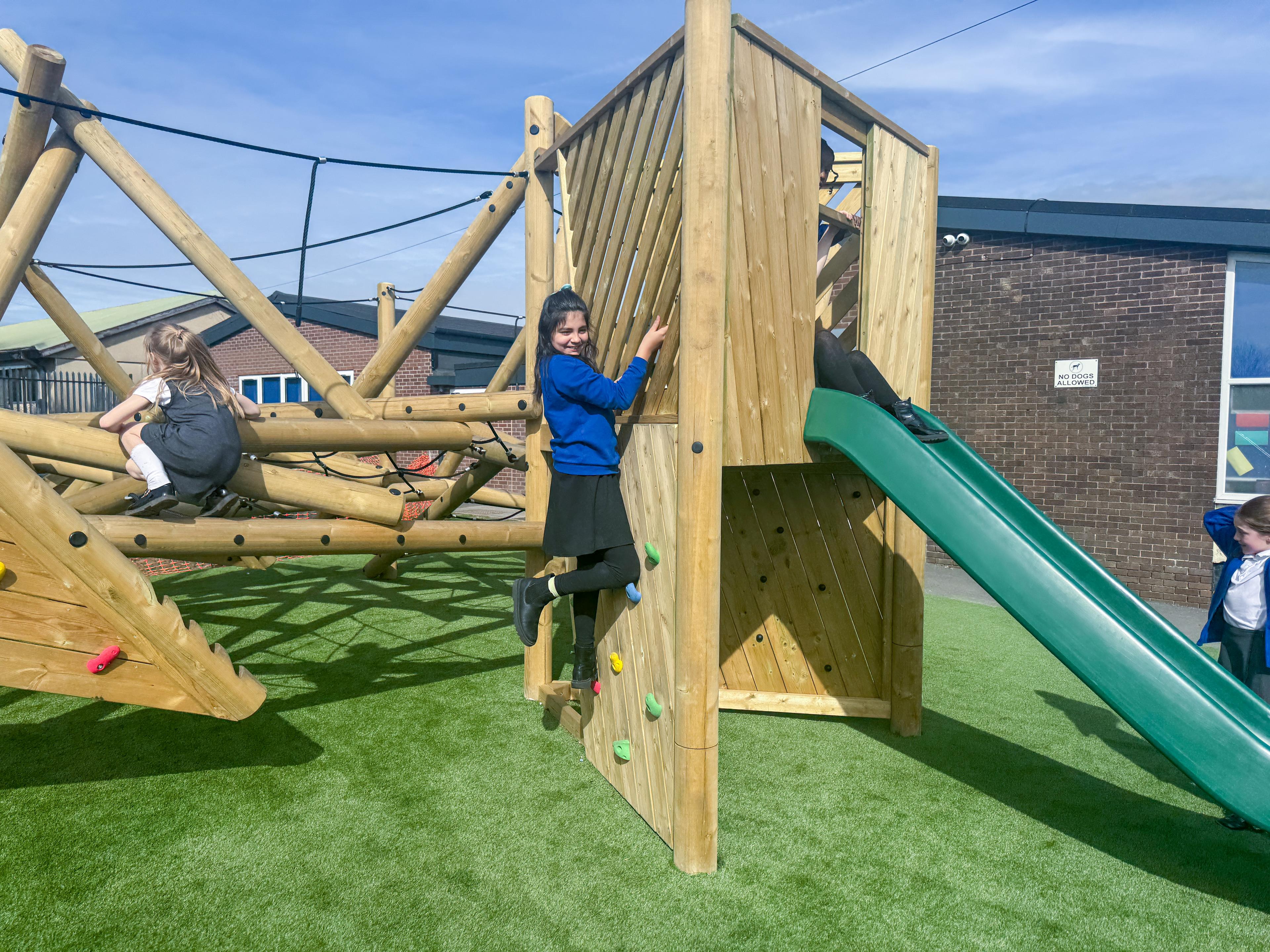 A girl climbing up a section of the play frame with climbing holds