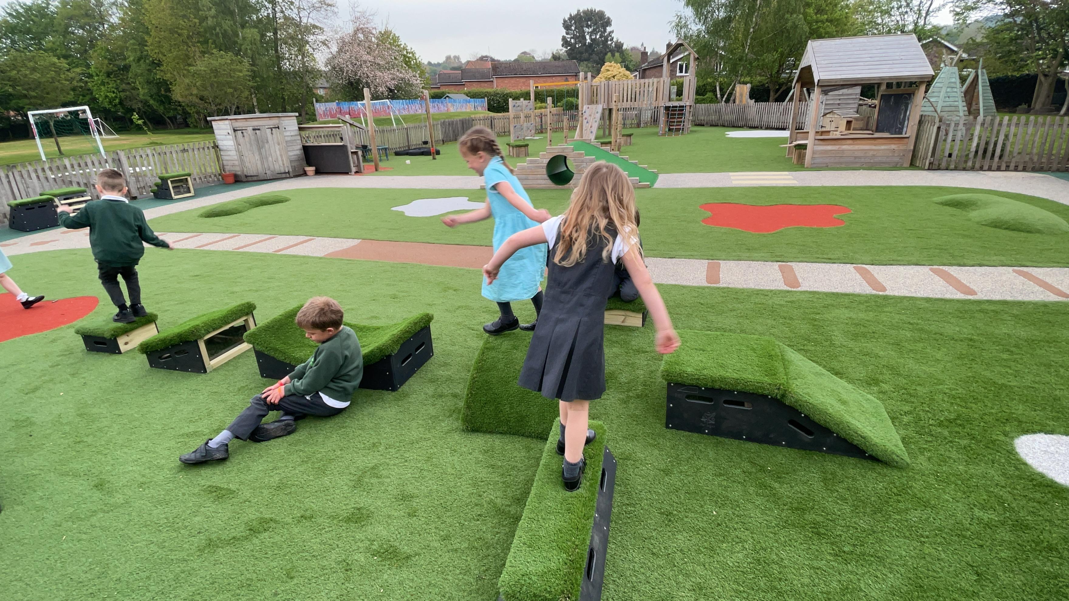 School children playing on grass-topped Get Set, Go! Blocks in the playground.