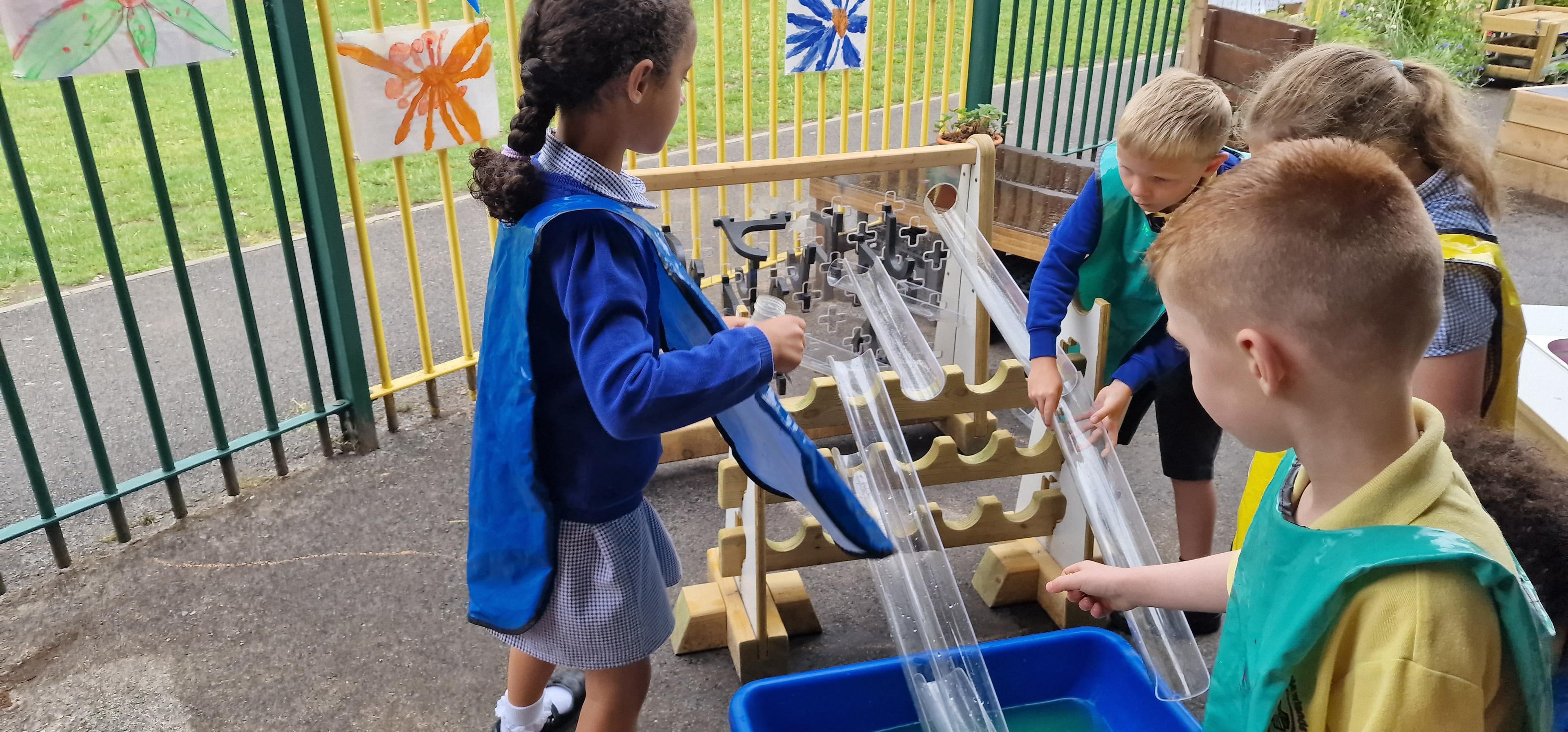 A girl and two little boys are constructing a track for the water to flow down with the channel stands and pipes.
