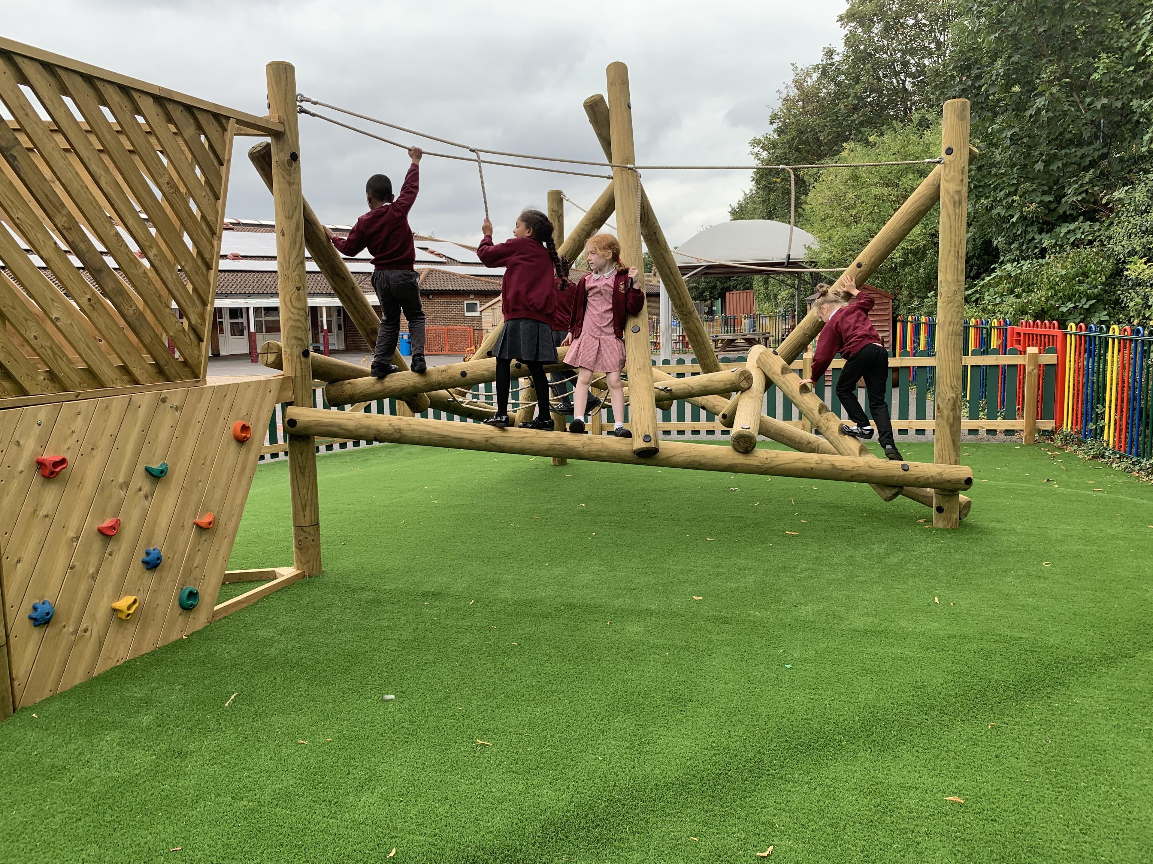 A group of KS1 children are climbing across a climbing frame towards an elevated platform.