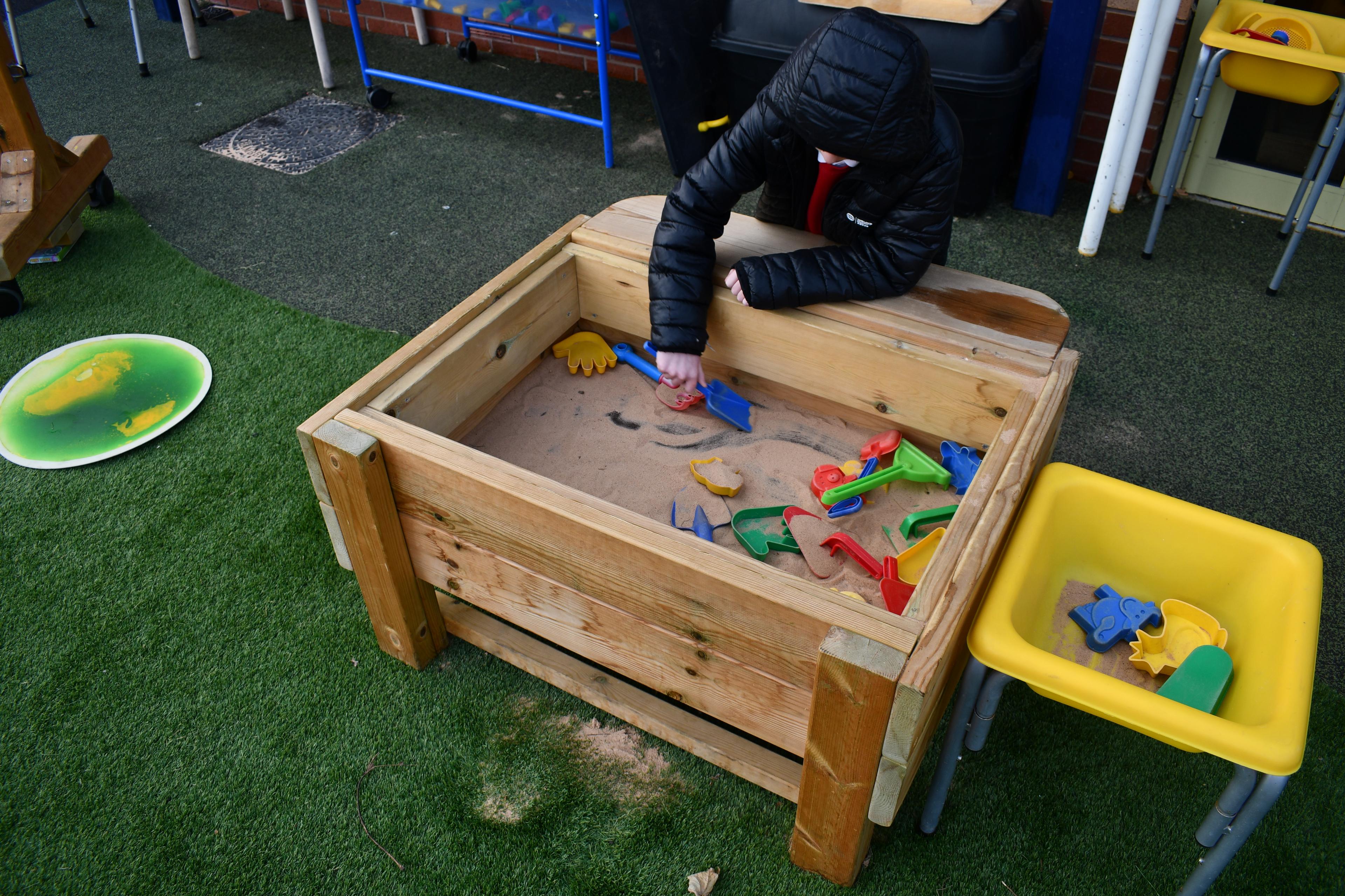 A close up of a boy's hand digging in the Pentagon Play Sand Table