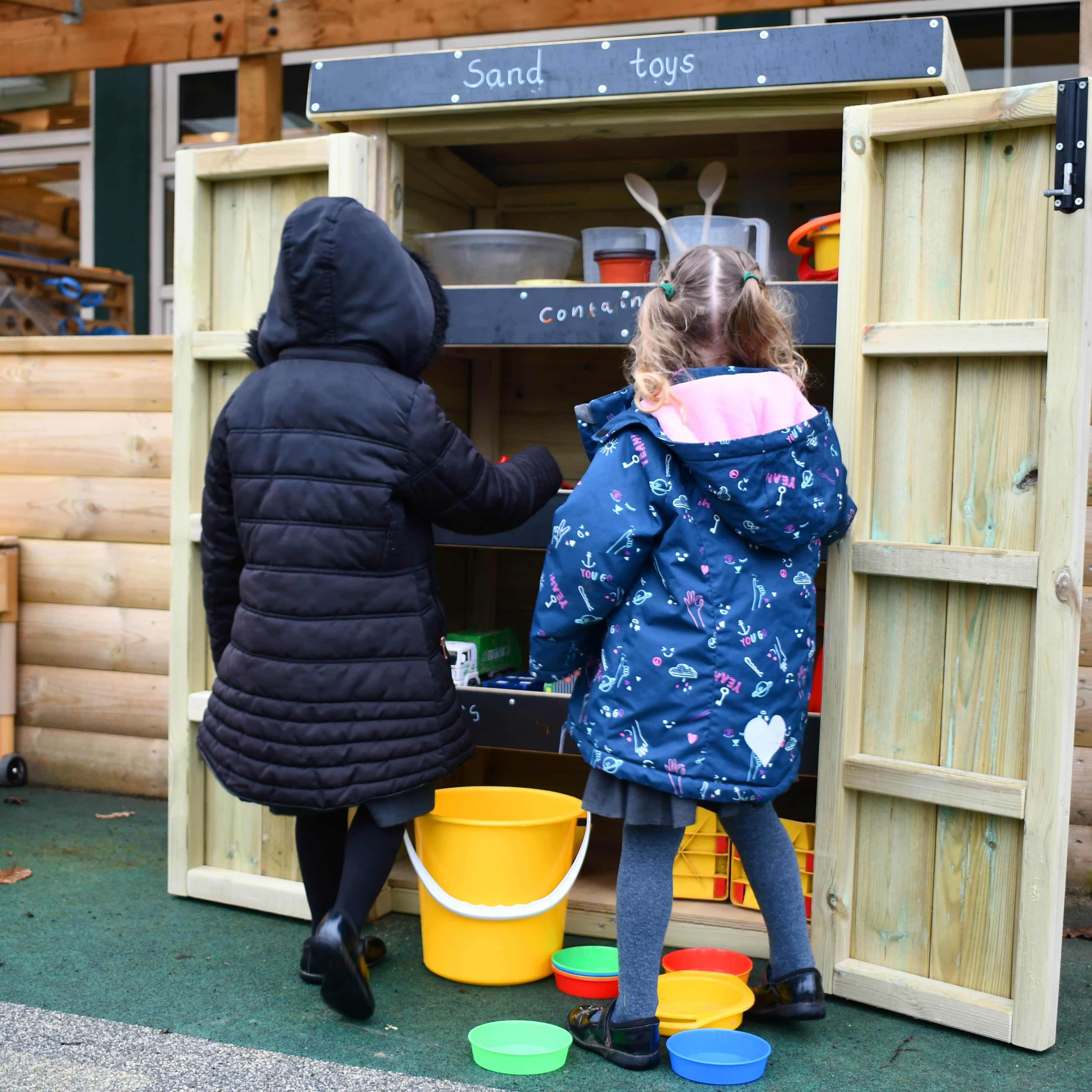 Two school children getting resources out of a Wooden Acorn Storage Unit in a school playground