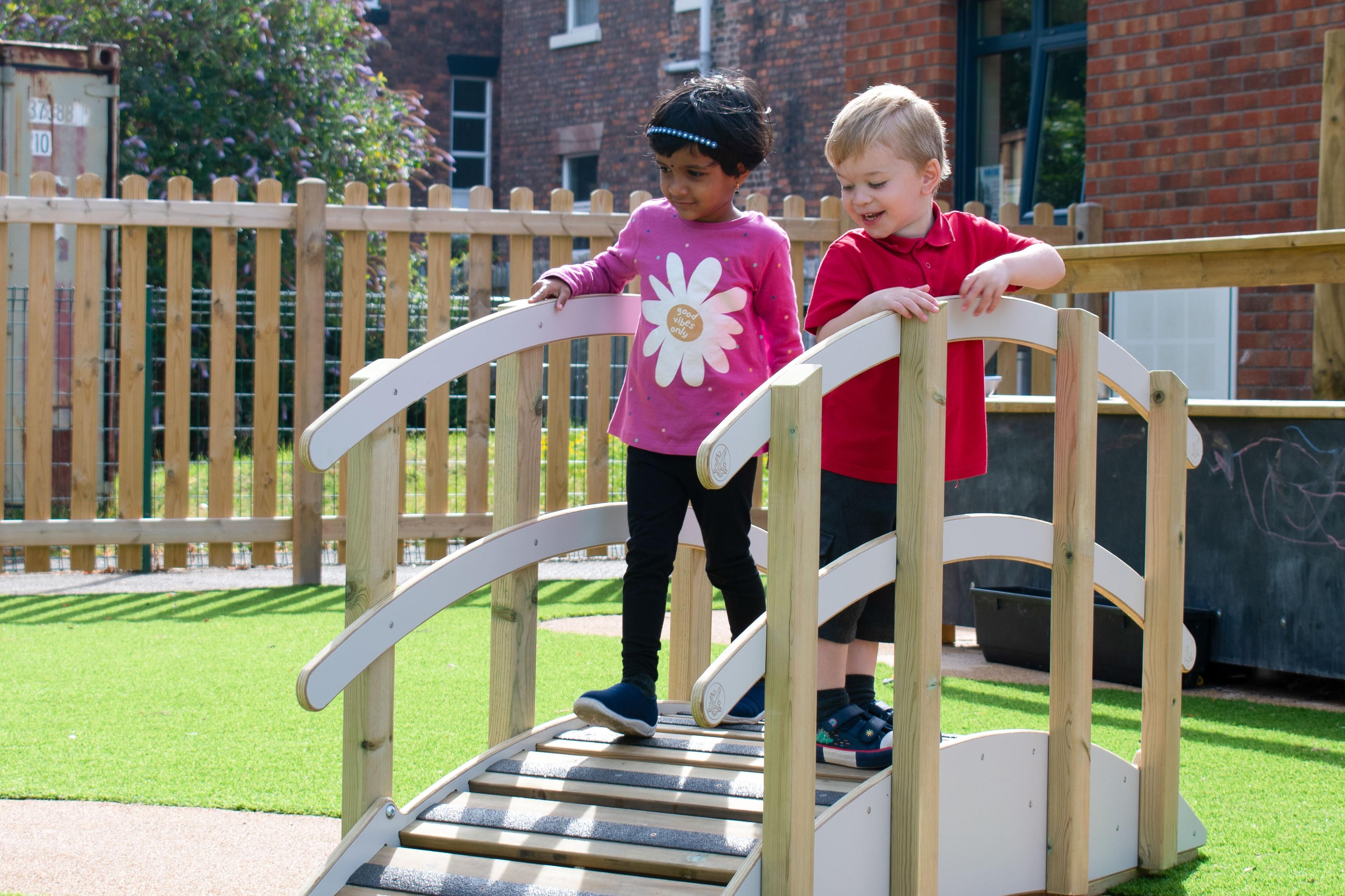 Two children are walking beside each other across the Play Bridge with Handrails.